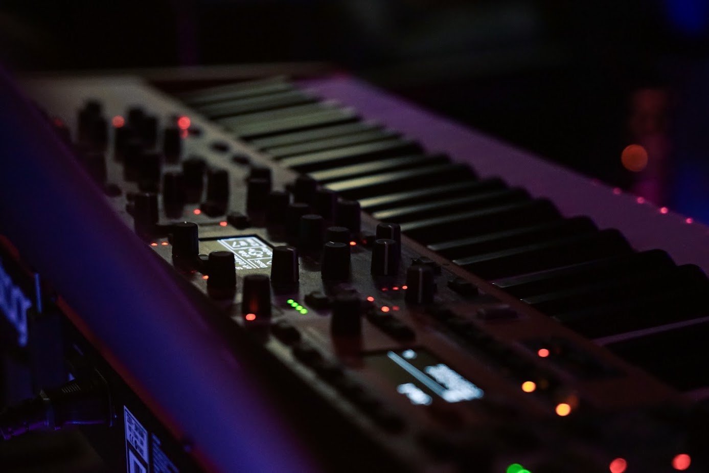 A close-up of a digital DJ mixer and keyboard illuminated with colorful lights in a dark setting.