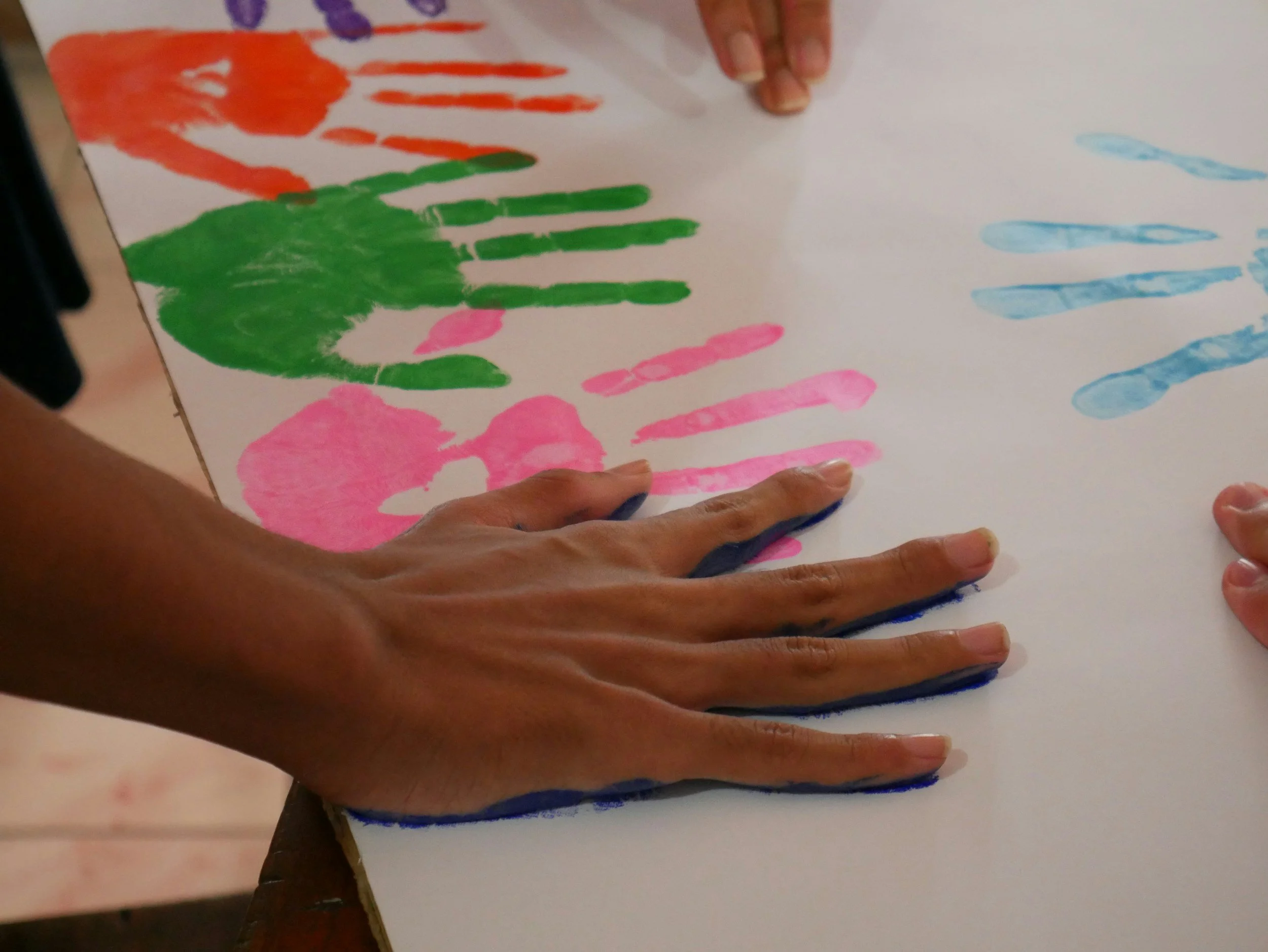 Colorful handprints and lines made with paint on a sheet of paper, being held and completed by hands.