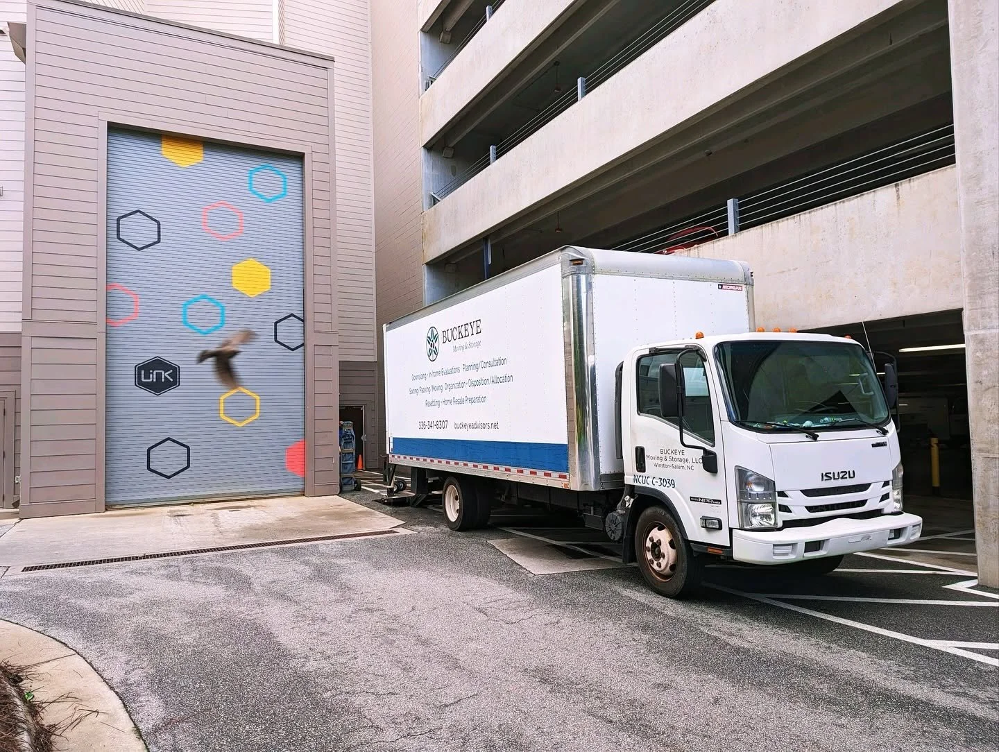 A moving truck parked outside a multi-story parking garage with a colorful geometric mural.