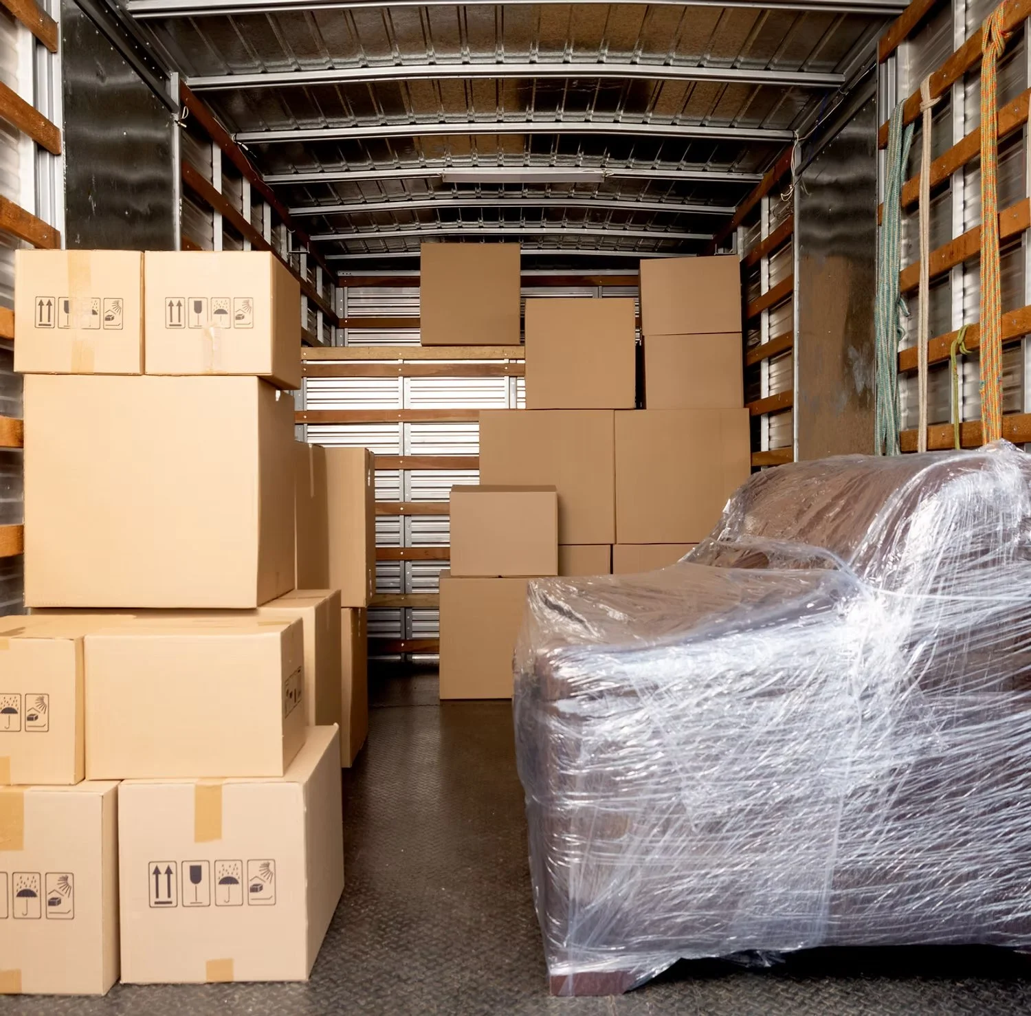 Inside a truck storage unit filled with stacked cardboard boxes and a piece of furniture wrapped in plastic.