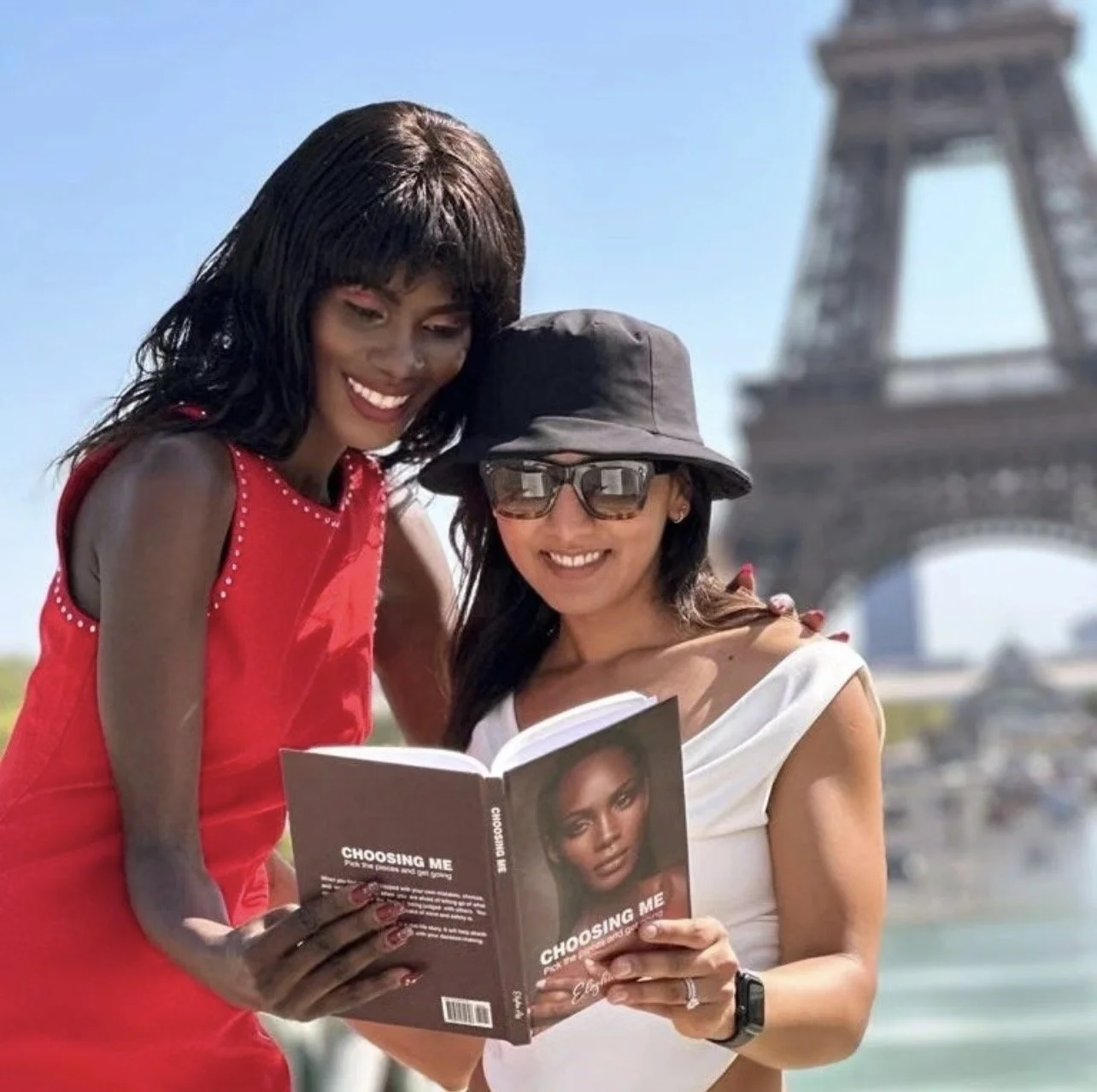 Two women smiling and reading ' Choosing Me' by Eleshia Ais outdoors with the Eiffel Tower in the background.