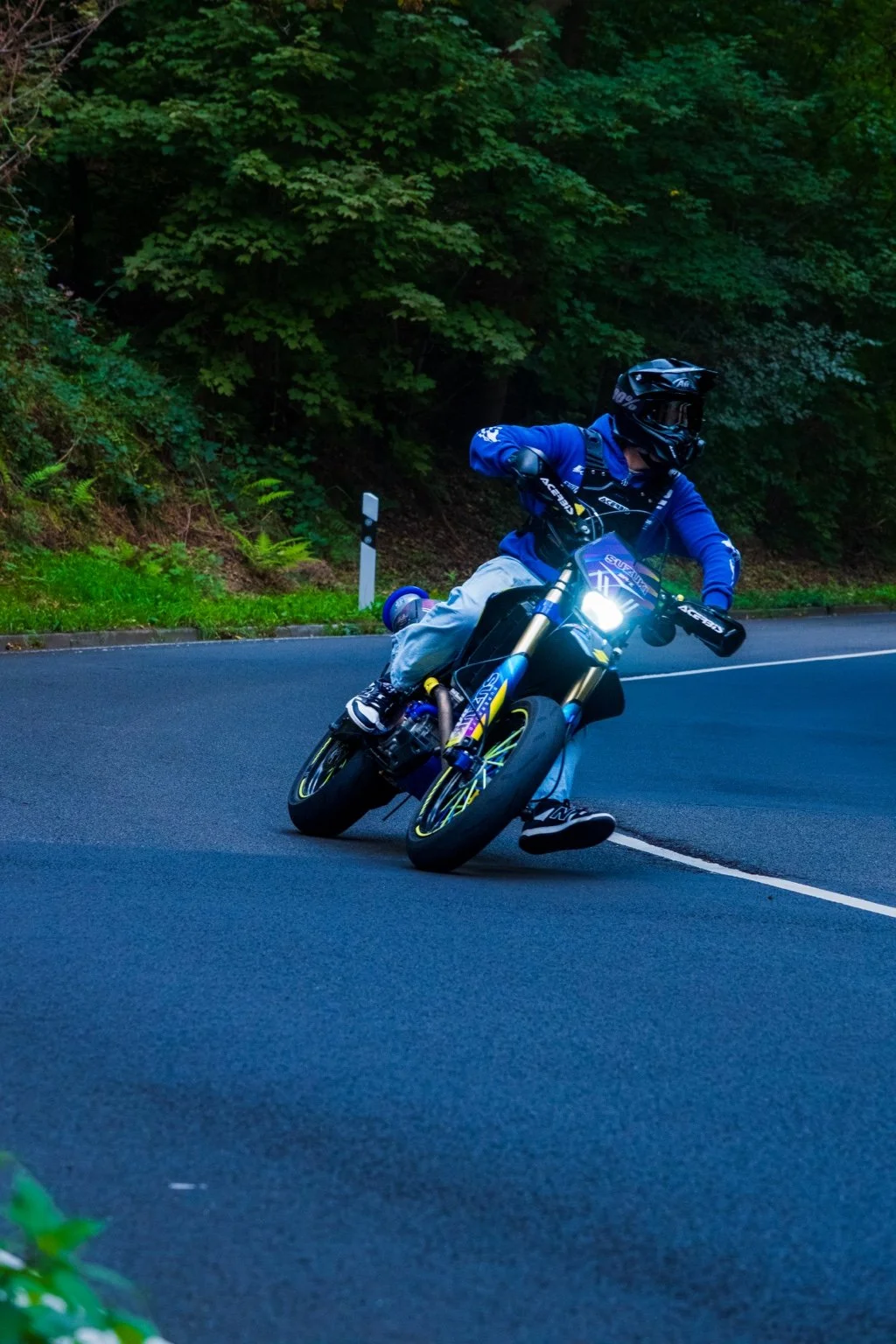 Motorradfahrer in dunkler Kleidung fährt kurvenreiche Straße, umgeben von grünem Baumbestand, während er eine Kurve nimmt.
