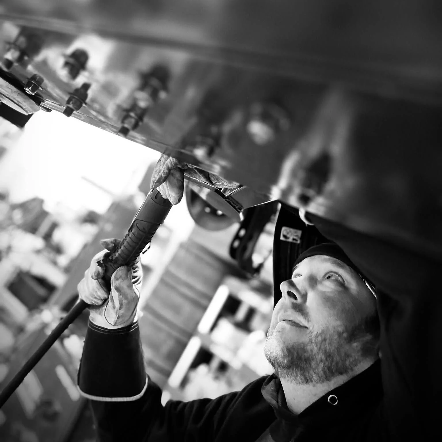 A man with a beard and wearing a baseball cap is working on a large piece of machinery, possibly welding or repairing, with a focused expression.