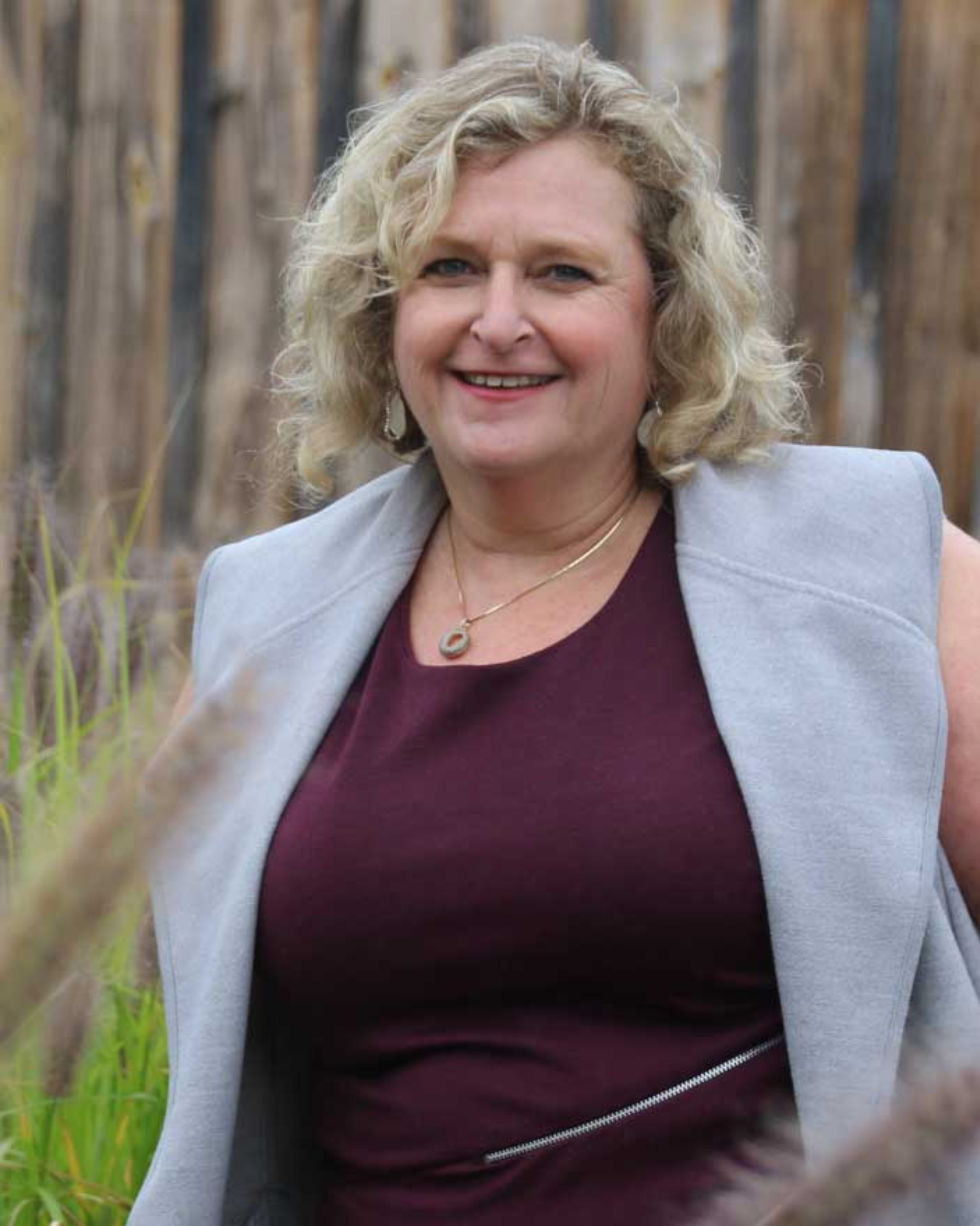 A headshot of Jill Kirson in a maroon shirt and grey vest sweater