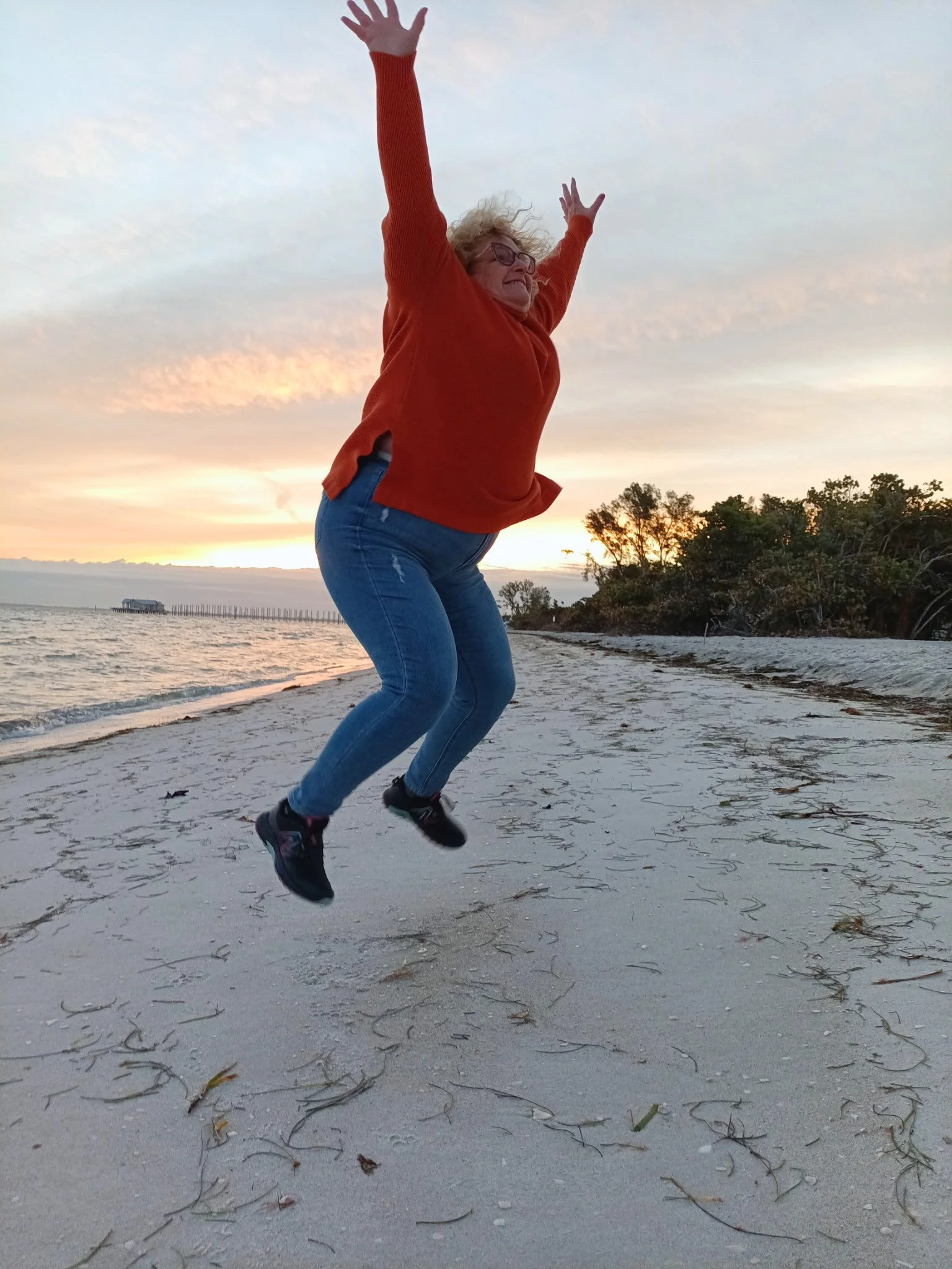An image of Jill jumping in joy on a beach during sunset