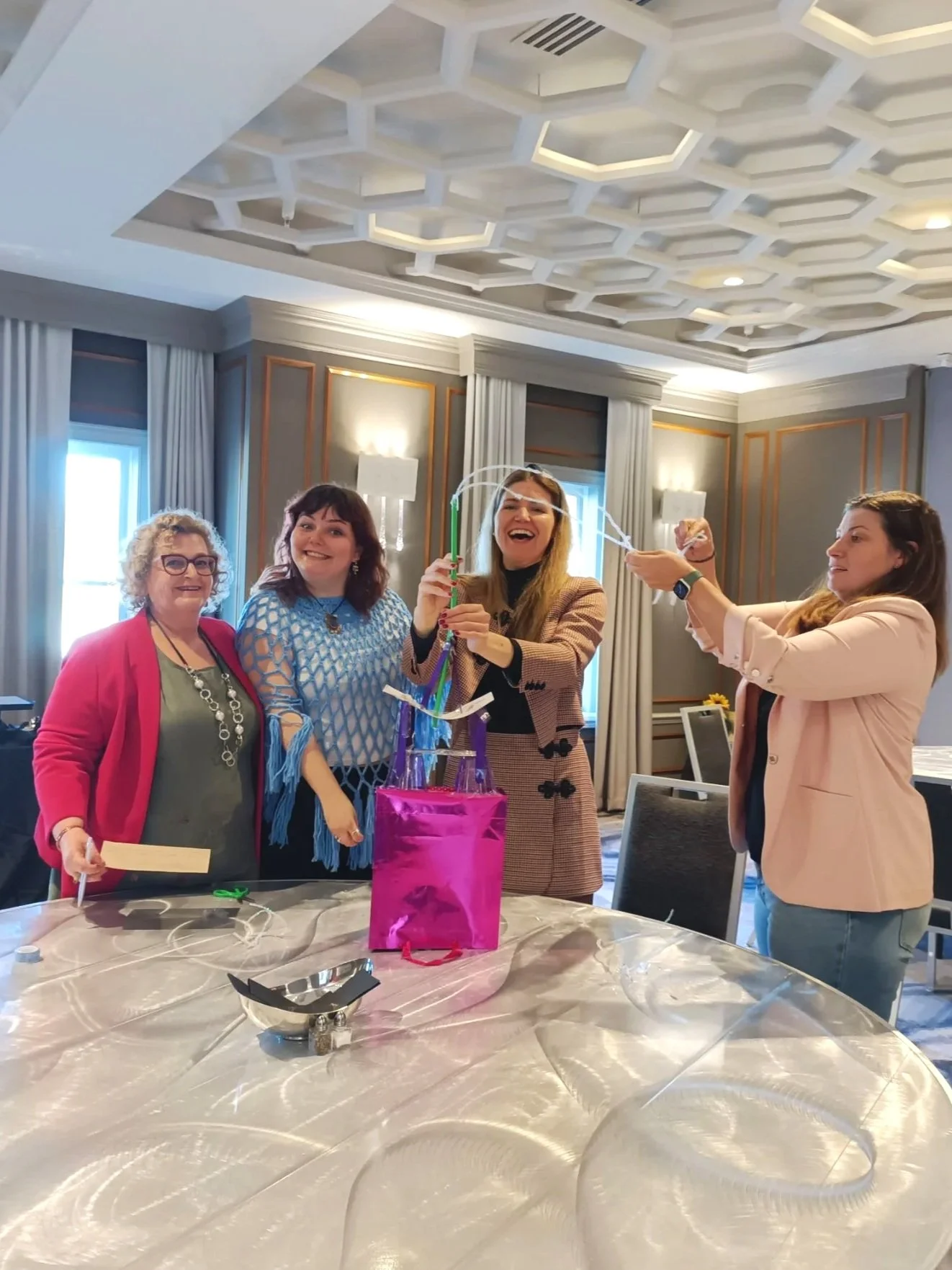 Four women smiling as they make a tower out of craft material on a table in a conference room