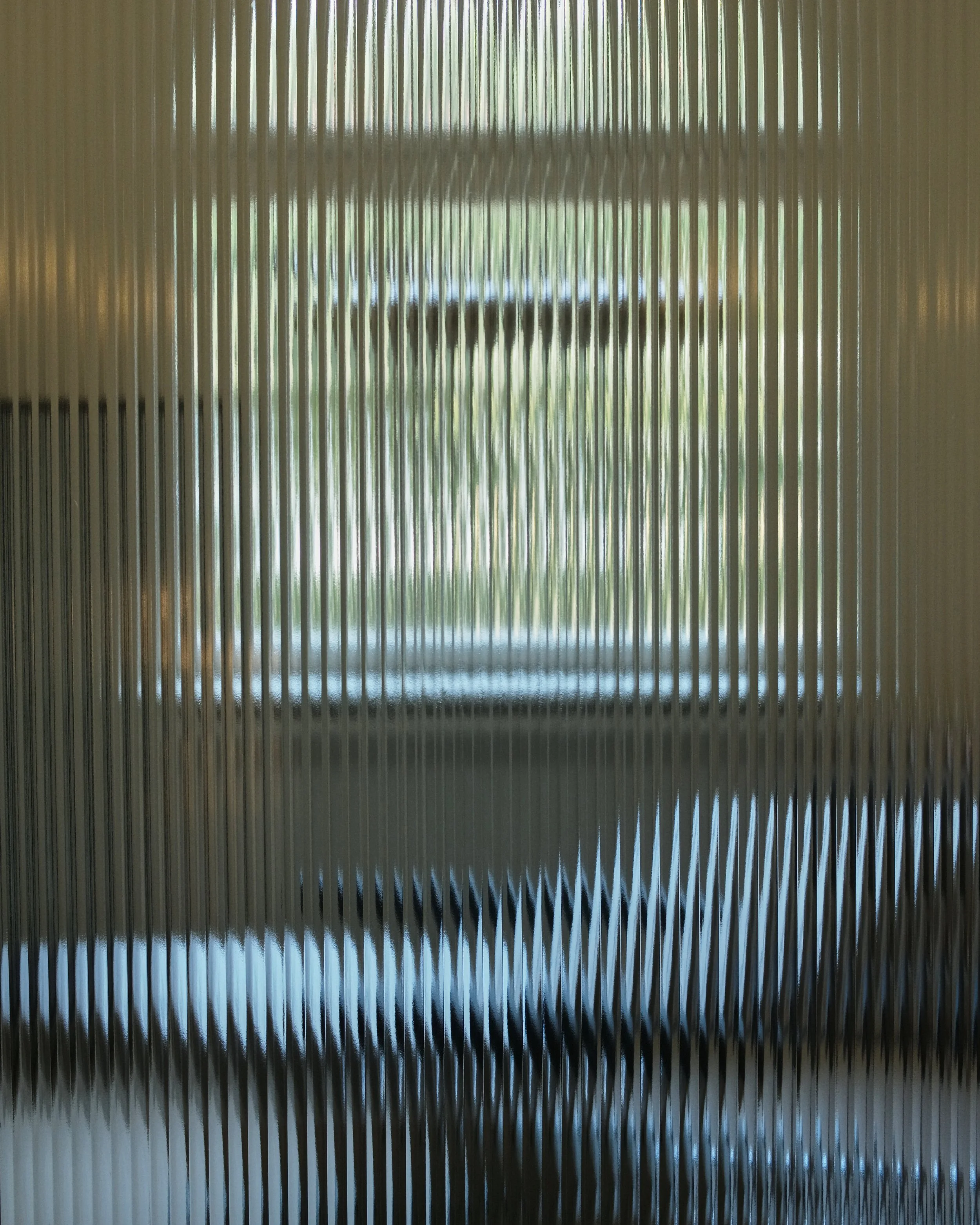 A corrugated metal surface with vertical ridges, showing reflections of trees and sky through the grooves.