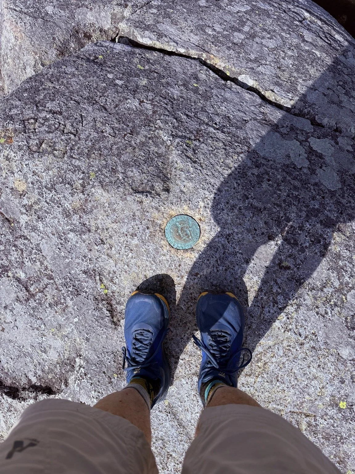 Bob Catinazzo’s hiking shoes beside a trail marker on a rocky summit.