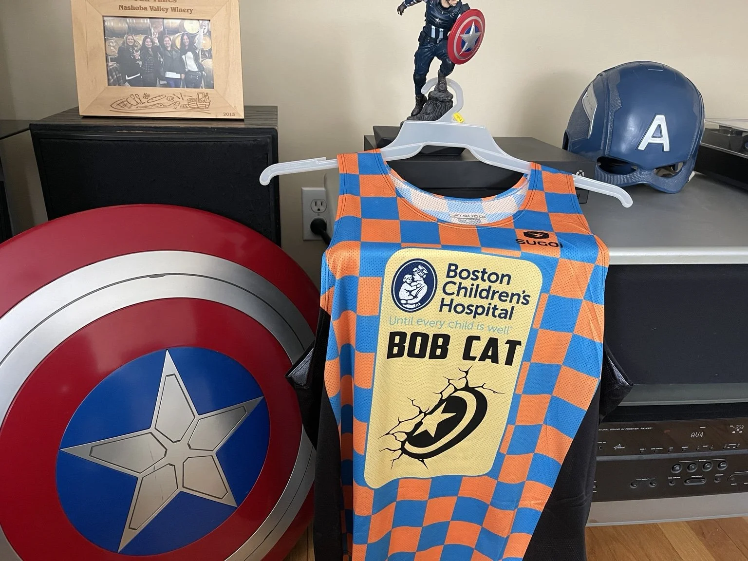 Boston Children’s Hospital running singlet displayed beside a Captain America shield.