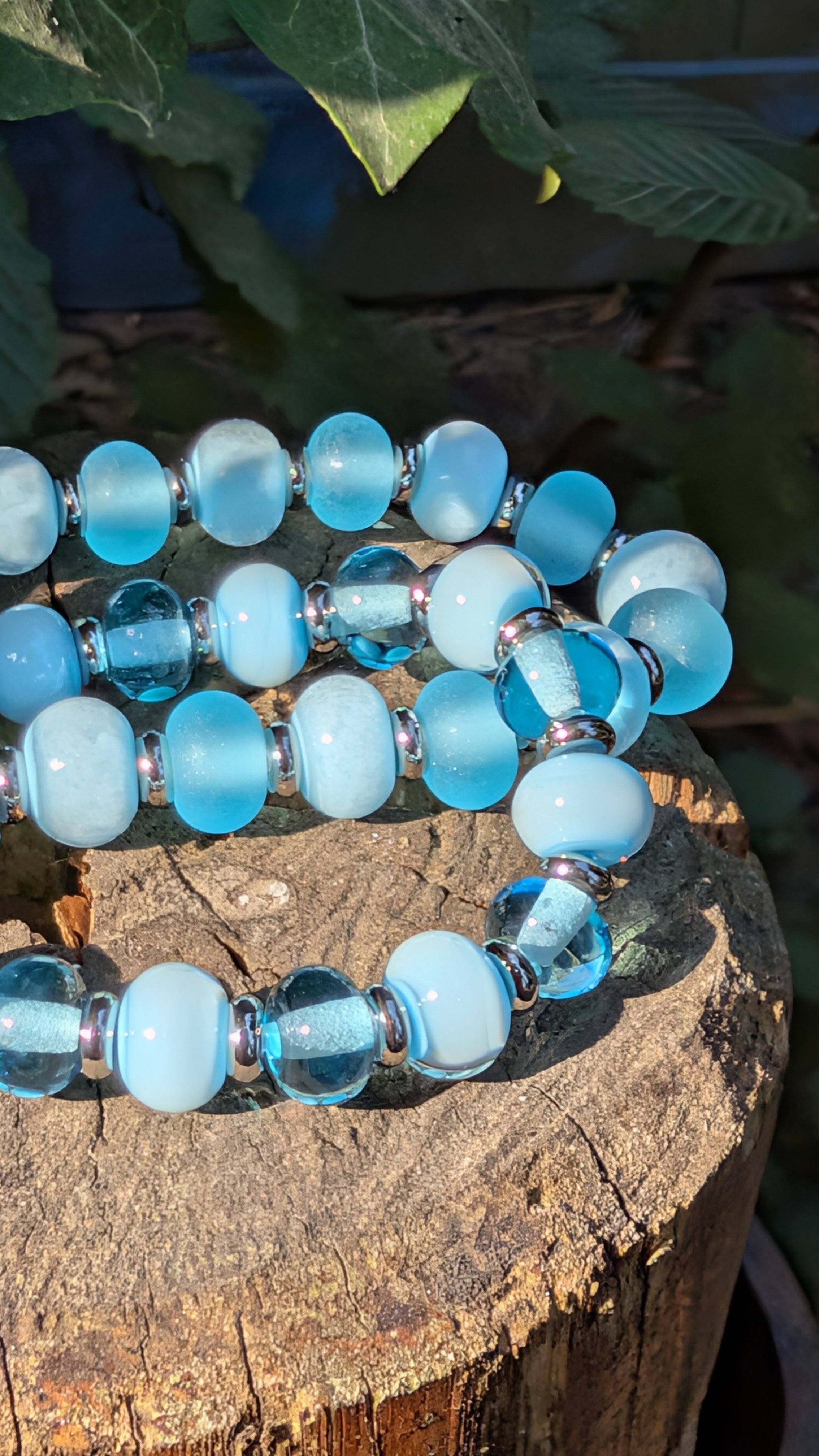 Bracelet en perles bleues et translucides posé sur un tronc d'arbre.