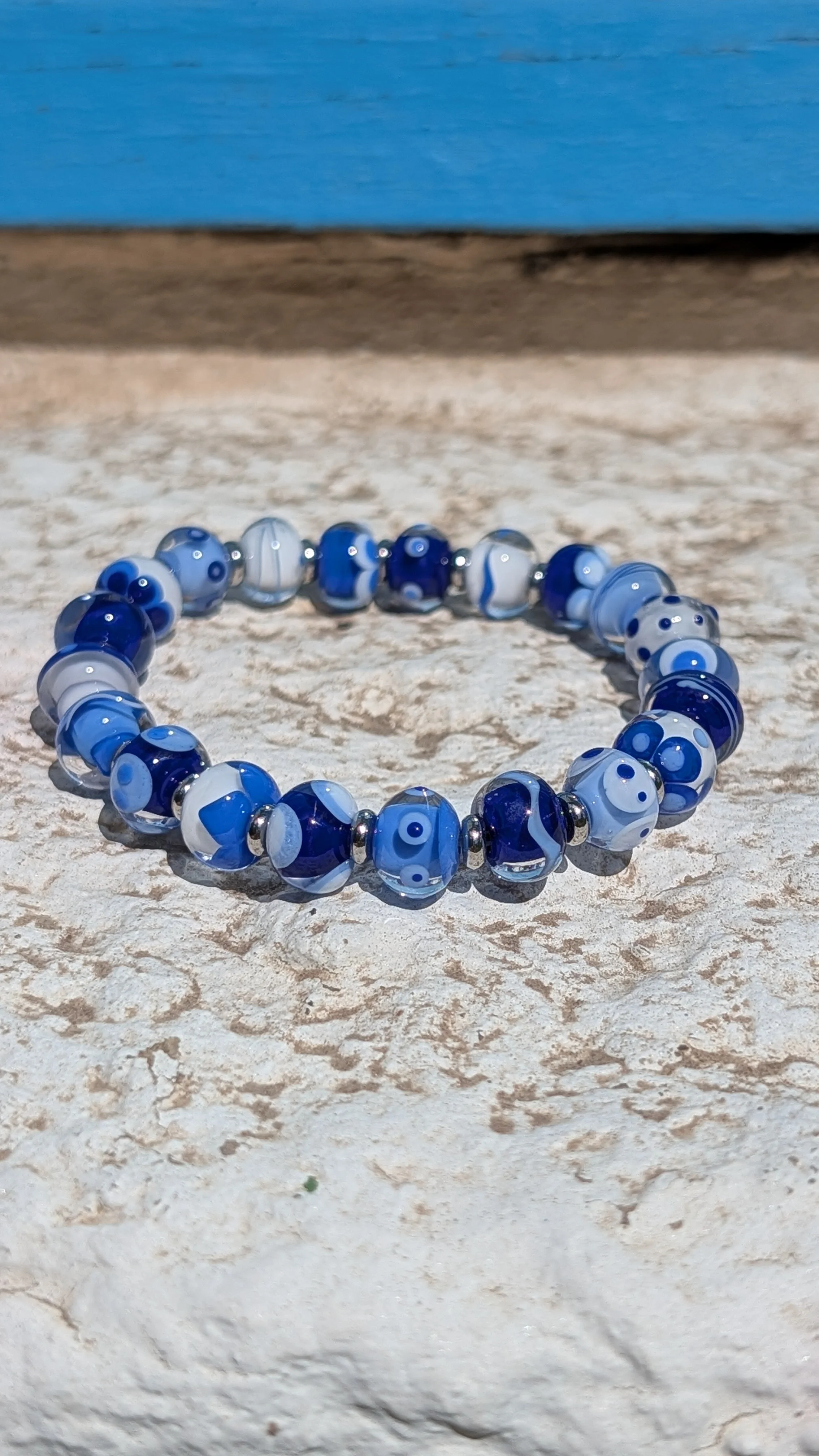 Bracelet en verre avec des perles bleues et blanches, posé sur une surface rocheuse.