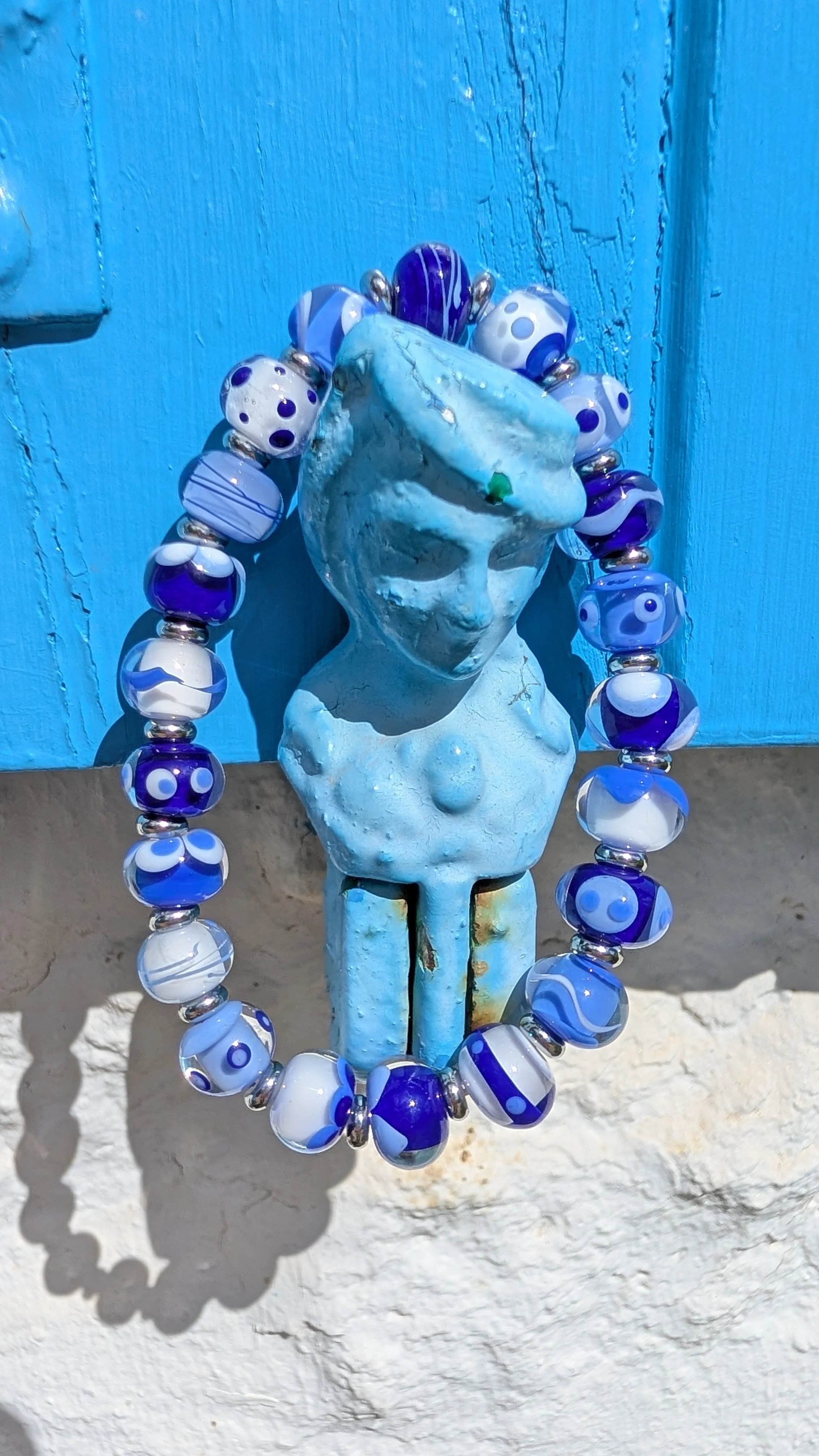 Une bust d'une femme en céramique bleue, entourée d'un collier de perles en verre bleu et blanc, fixé à un mur bleu en bois.