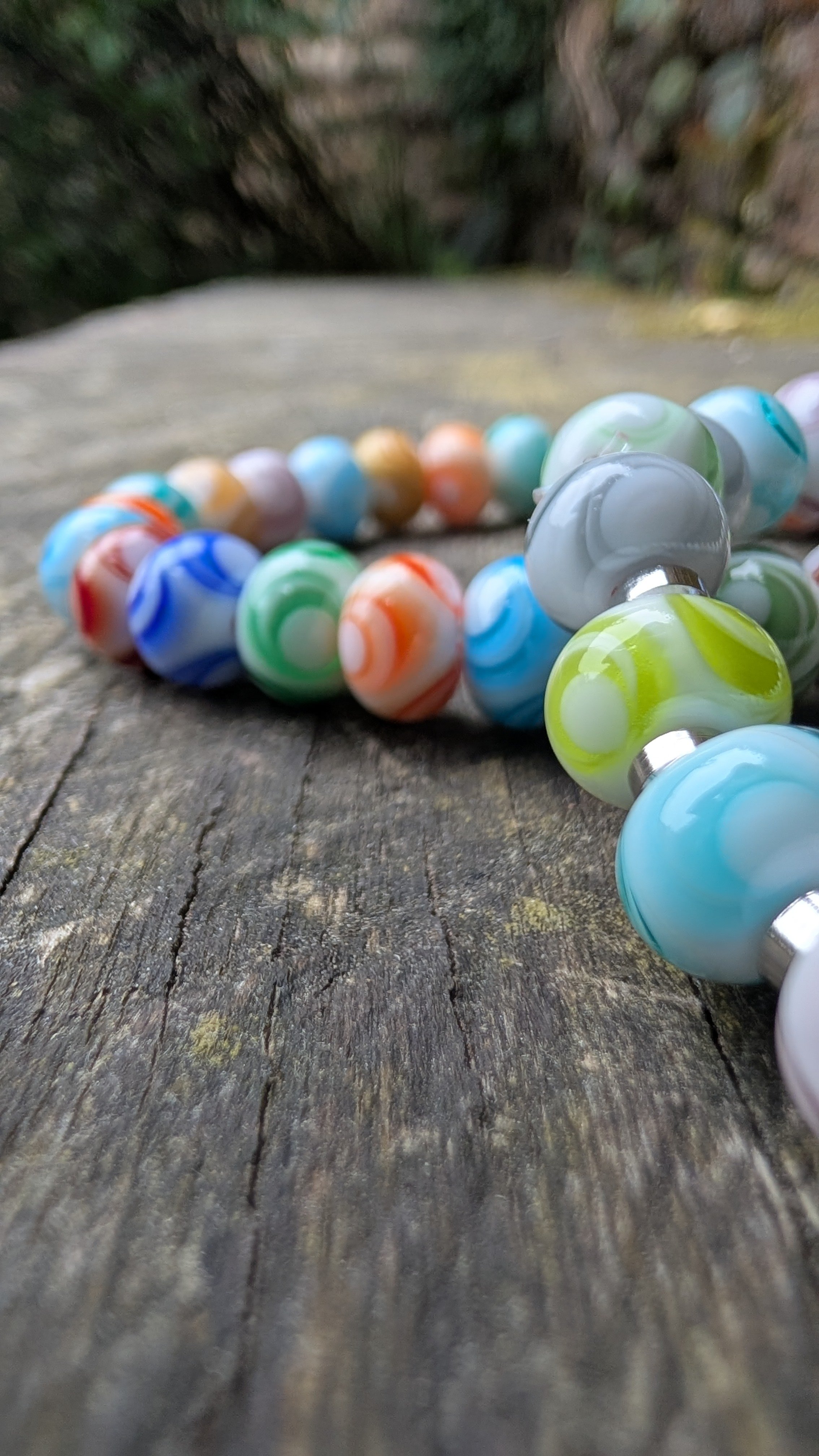 Bracelet de perles colorées posé sur une surface en bois, avec un fond de végétation floue.
