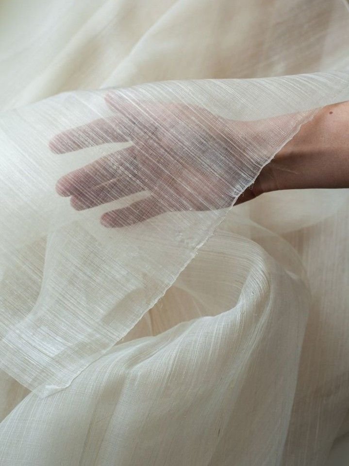A hand holding transparent, lightweight fabric or sheer material, with a soft, beige background.