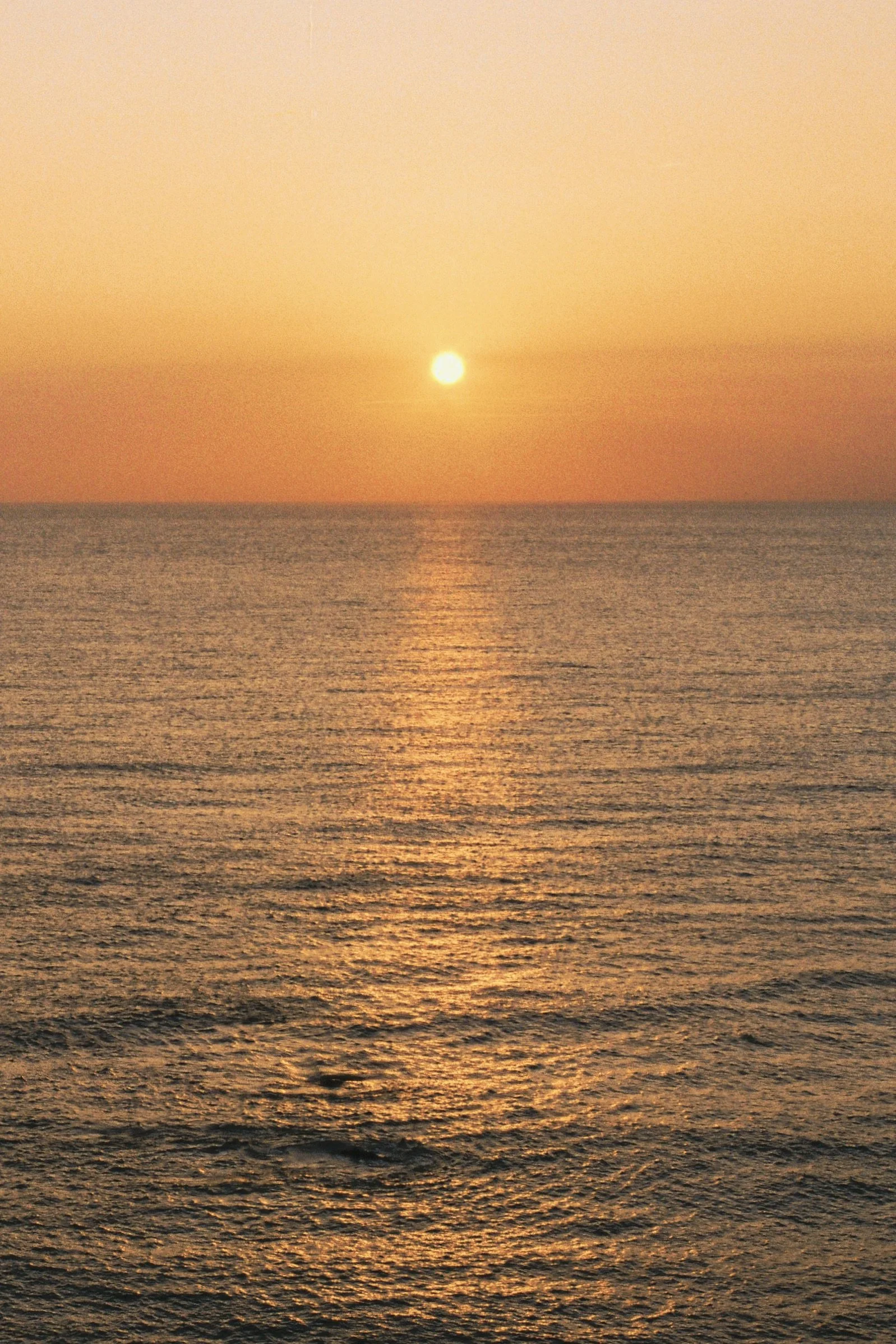 Sun setting over the ocean with a golden reflection on the water.