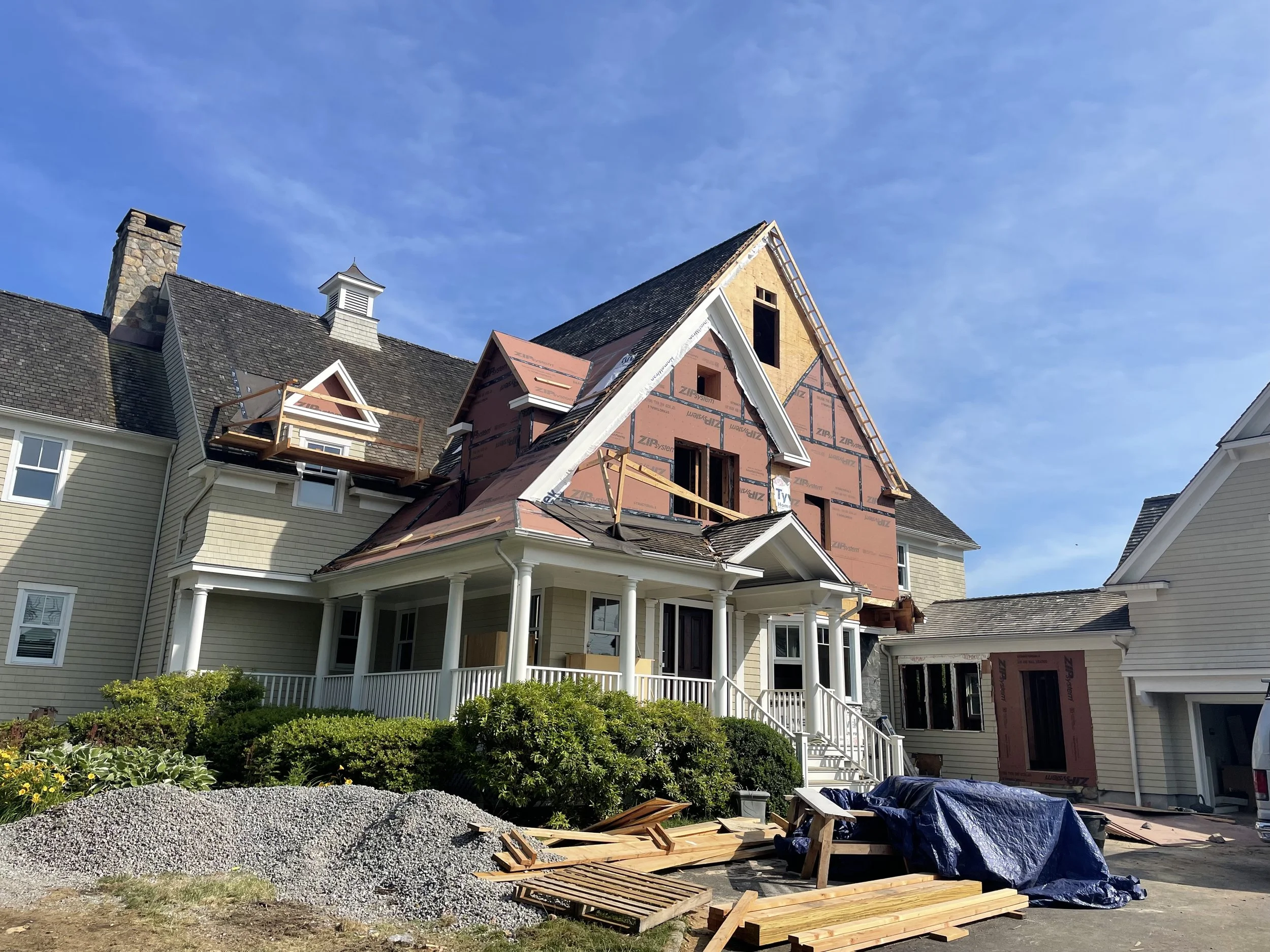 House under renovation with construction materials and debris in front, scaffolding on the roof, and an unfinished attic area.