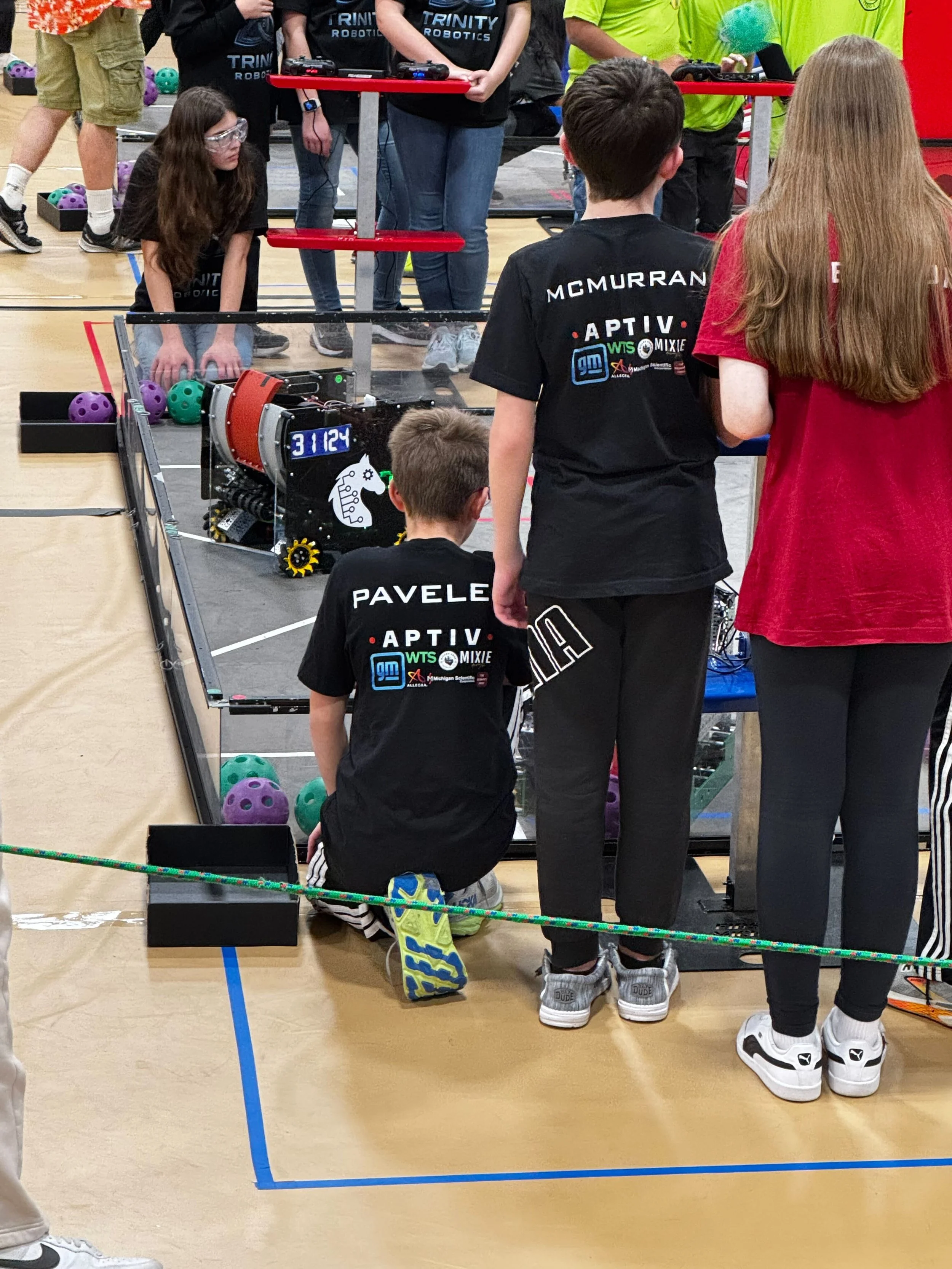 Young students competing in a robotics competition in a gymnasium, working on a robot with a digital display showing '31124'.