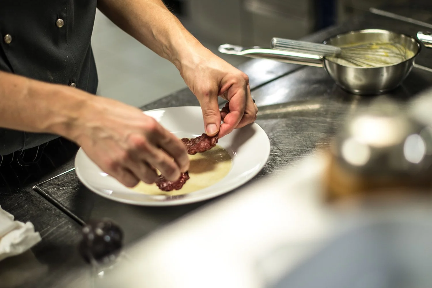 Koch bereitet ein Gericht vor, indem er Fleisch in eine Sauce auf einem weißen Teller taucht.