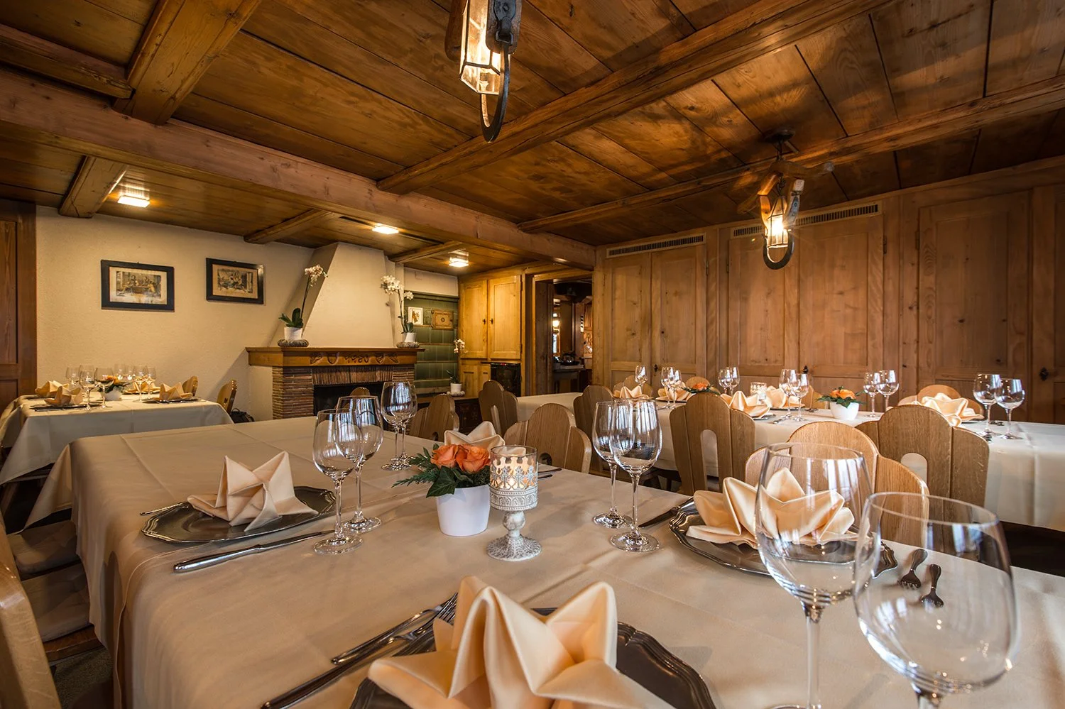 Eleganter, festlich gedeckter Speiseraum mit Holzwänden und -decke, Kerzen, Blumen und Gläser auf Tischen