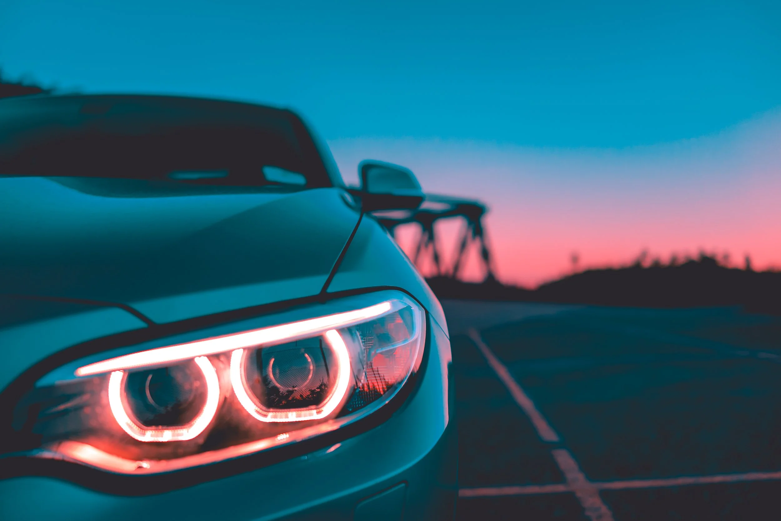 Close-up of a car's taillight at dusk, with a blurred background of a bridge and a colorful sky.