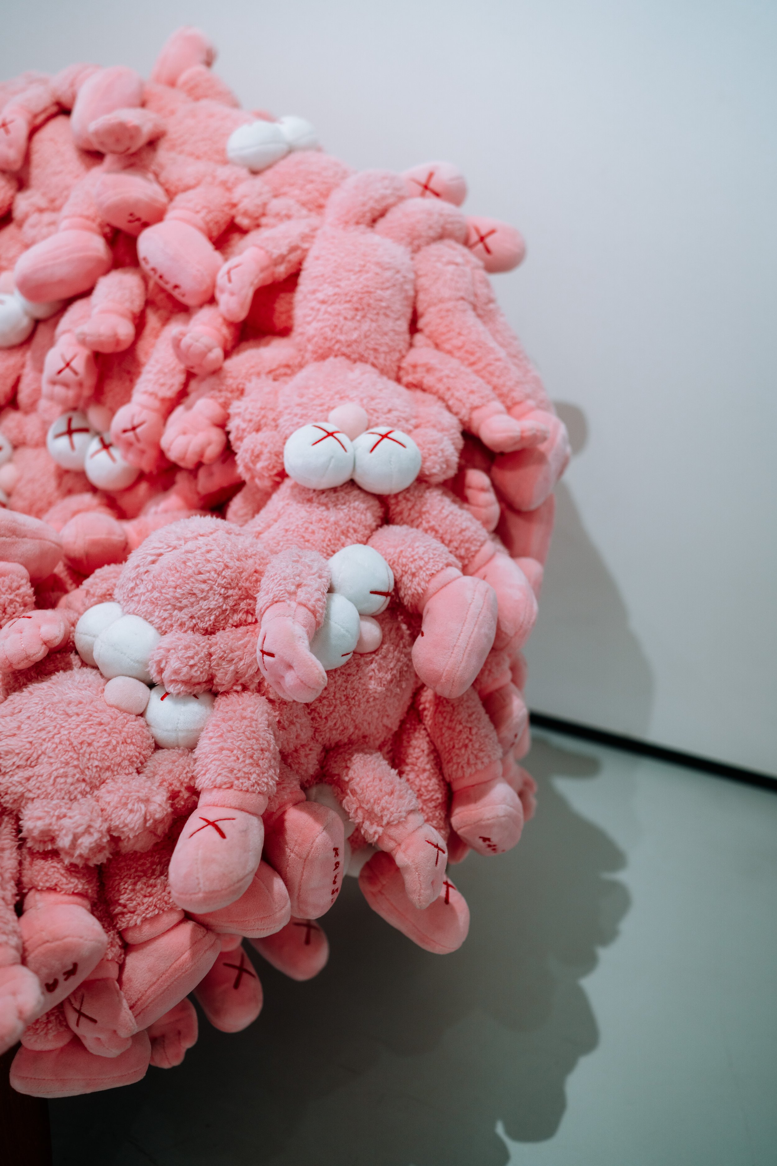 Close-up of a pink plush toy with multiple limbs and white stuffed balls with red crosses on them, arranged in a cluster on a gray surface.