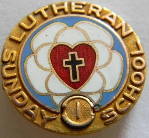 Religious membership pin with a gold border, featuring a heart with a cross, surrounded by a floral design, and the words "Lutheran 100th Day" and the number "1".