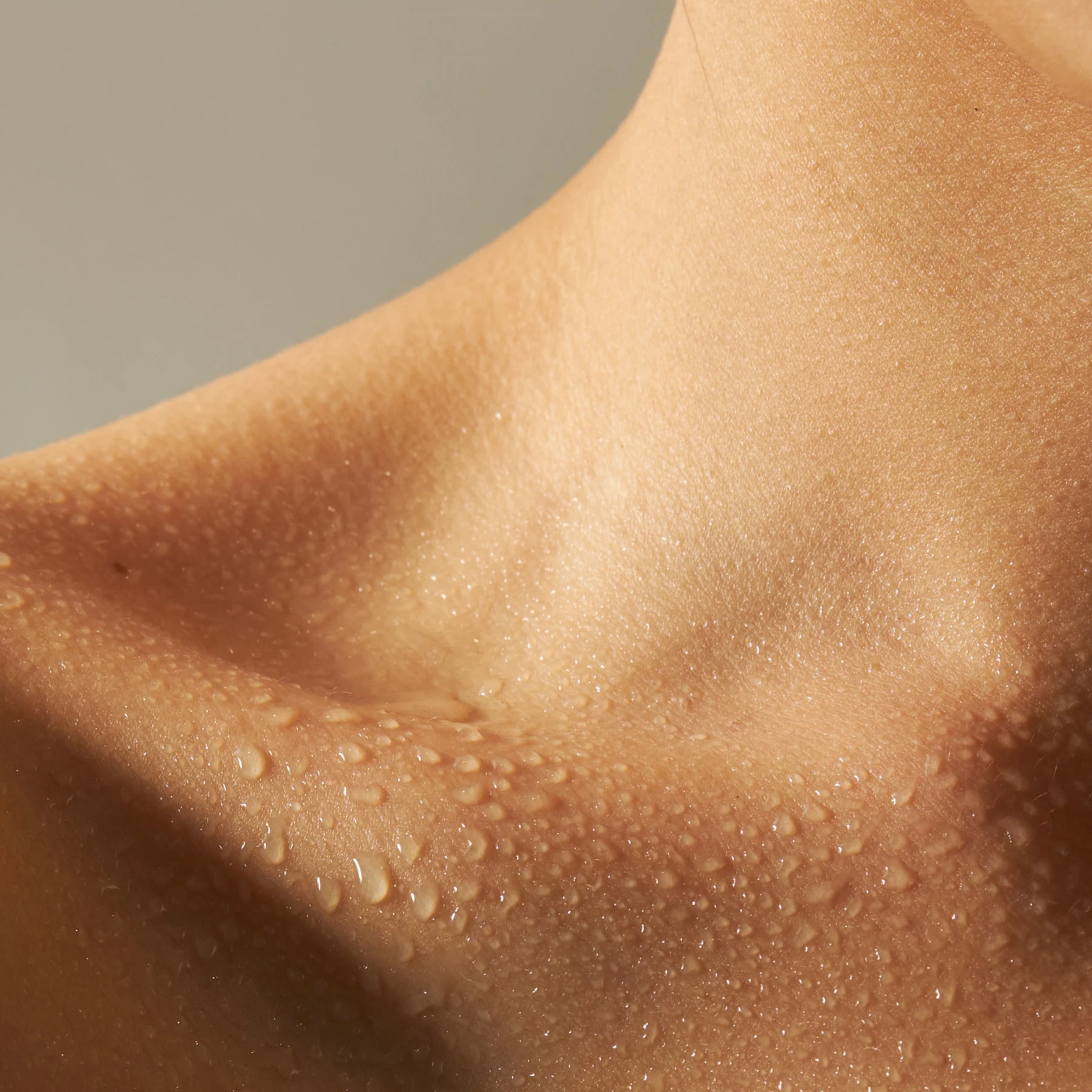 Close-up of smooth, glowing skin on the neck and collarbone with water droplets.