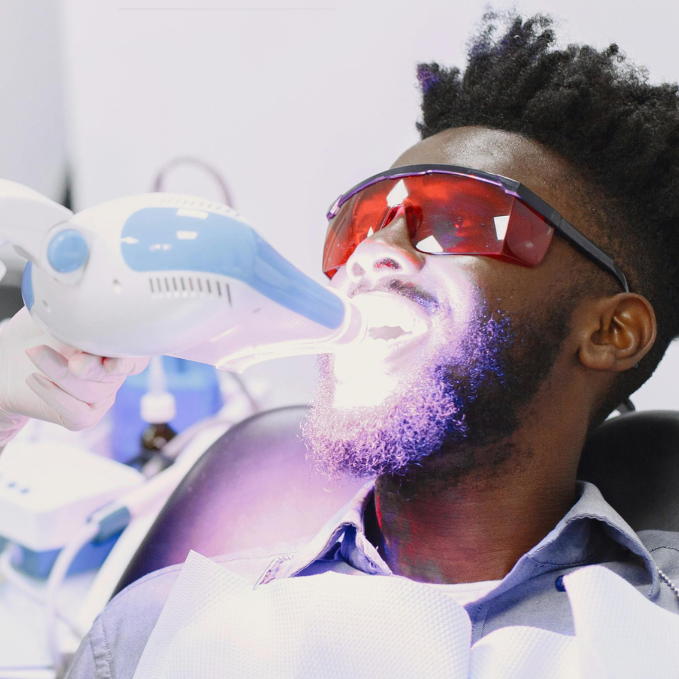 Client wearing protective eyewear while receiving a cosmetic teeth whitening treatment with an LED light positioned near the mouth.