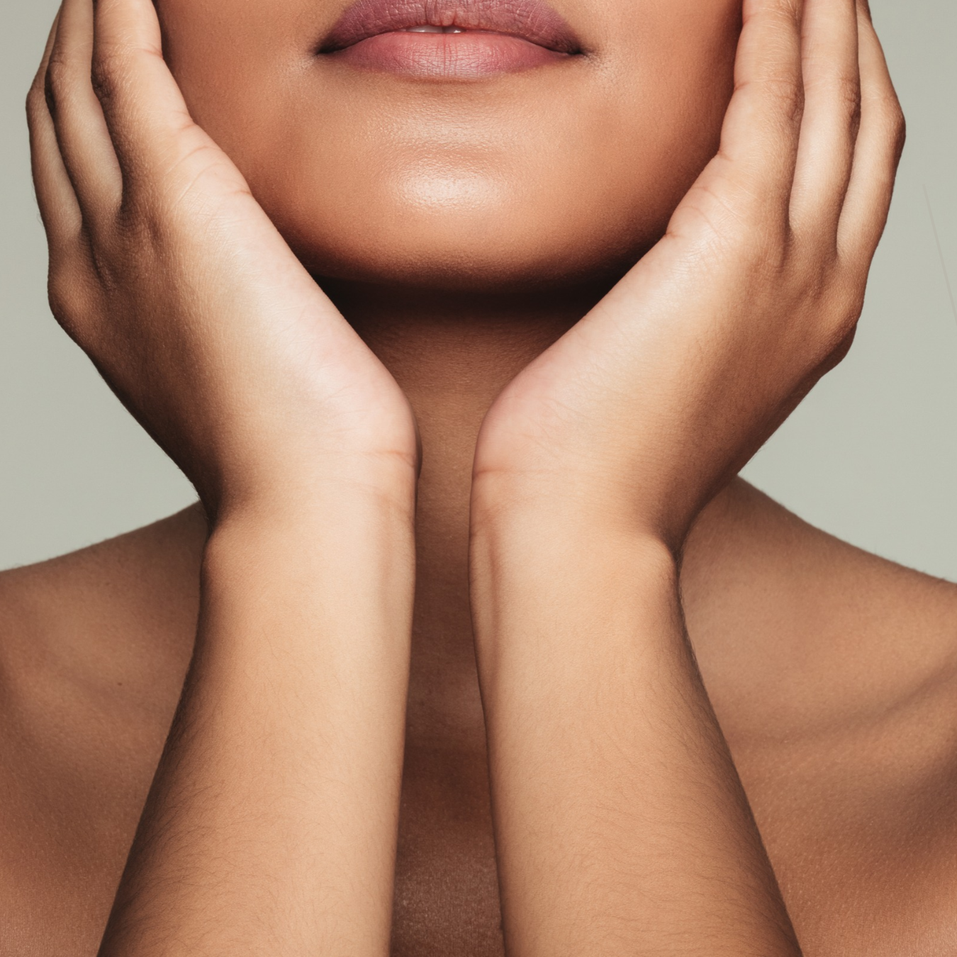 Close-up of a woman with smooth, radiant skin gently holding her face, representing the benefits of dermaplaning and microdermabrasion at Gloss'd Skin Studio in White Plains, NY.