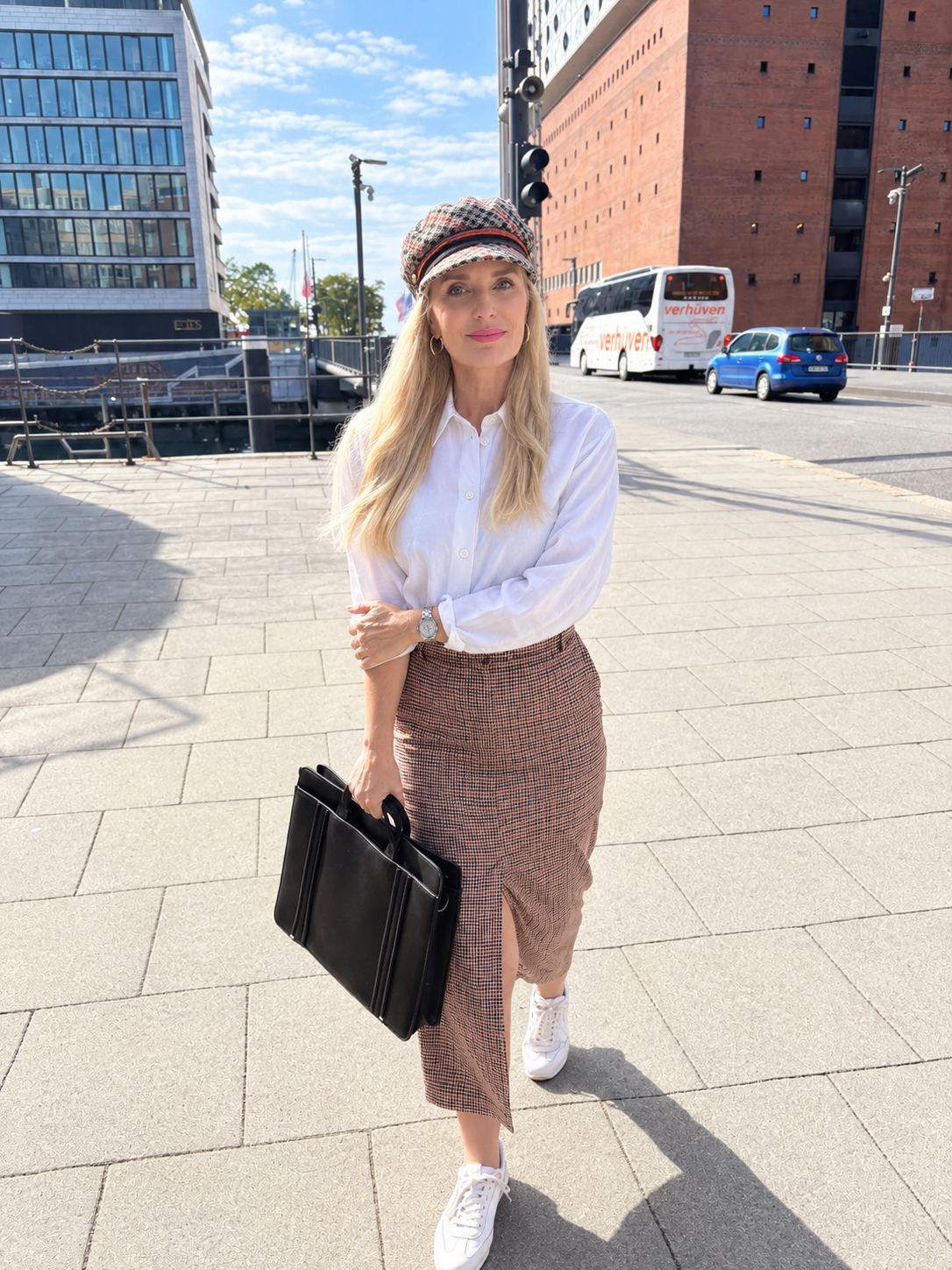 Marisa Ruiz walking through Hamburg, wearing a white blouse, long skirt and checked cap.