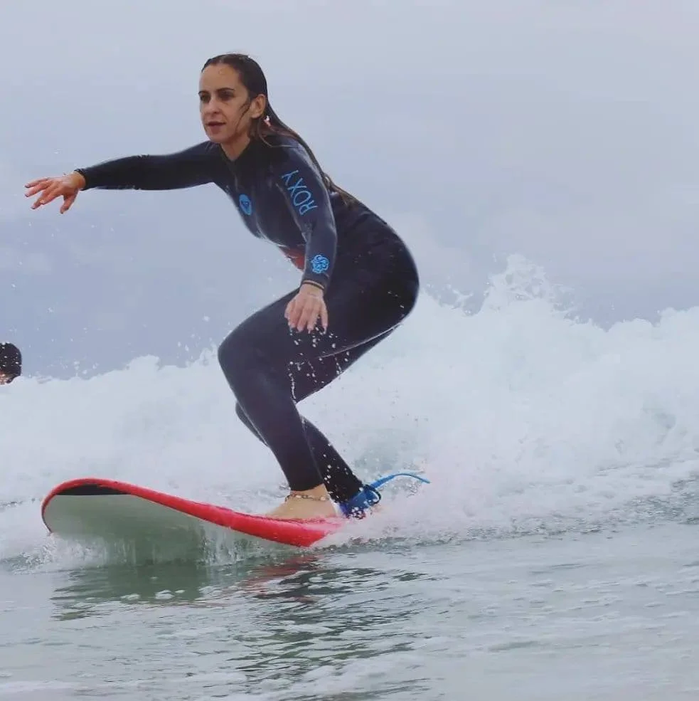 A woman surfing on a wave while wearing a black wetsuit with blue lettering.