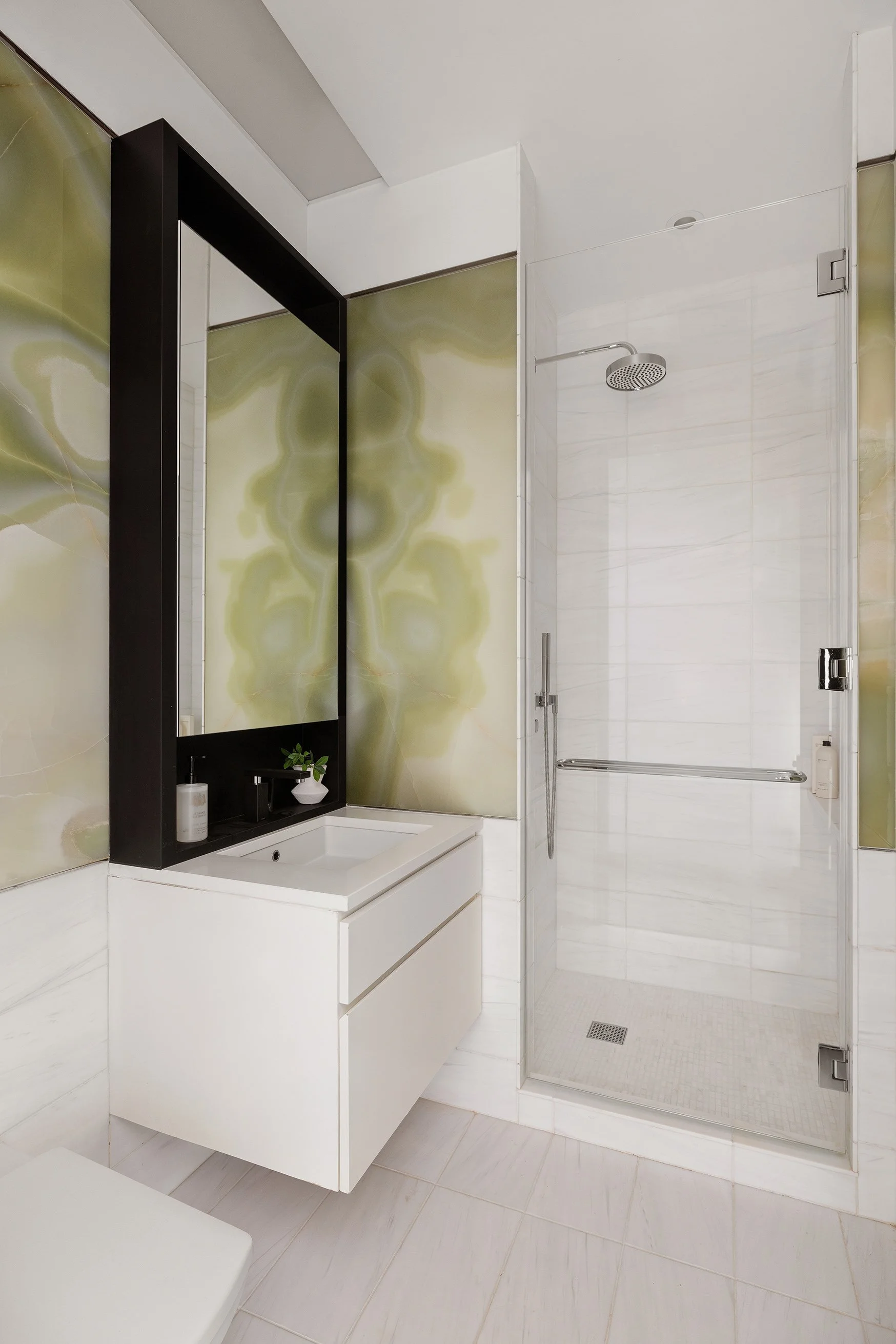 Modern bathroom with a walk-in shower featuring a rain showerhead, a white vanity with drawers, a large mirror, and a green abstract design on the wall panels.