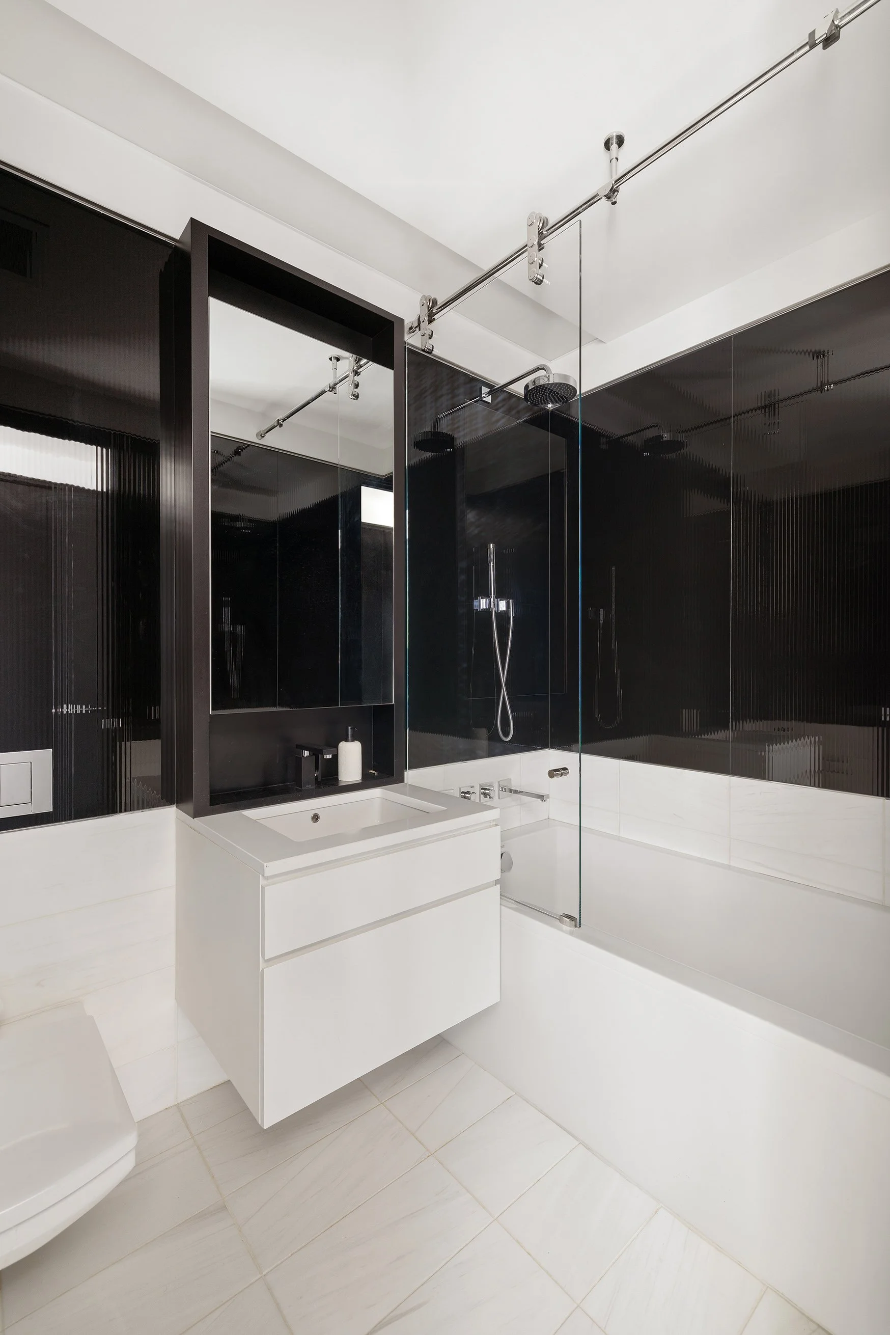 Modern bathroom with white vanity, black framed mirror, black wall panel, glass shower enclosure, and white tiled floor.