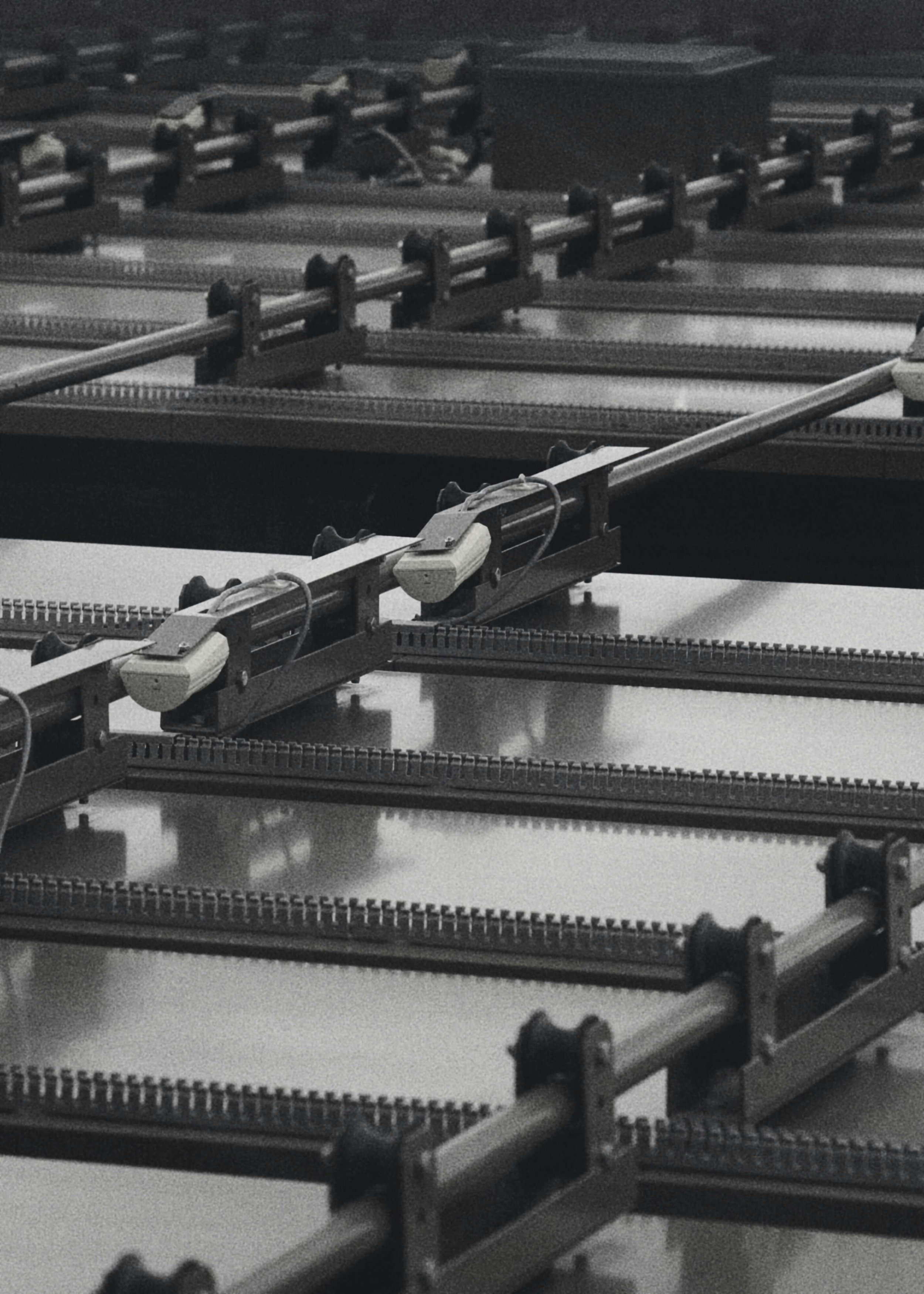 Black-and-white close-up of rows of industrial textile loom machinery with shuttles and metal rails.