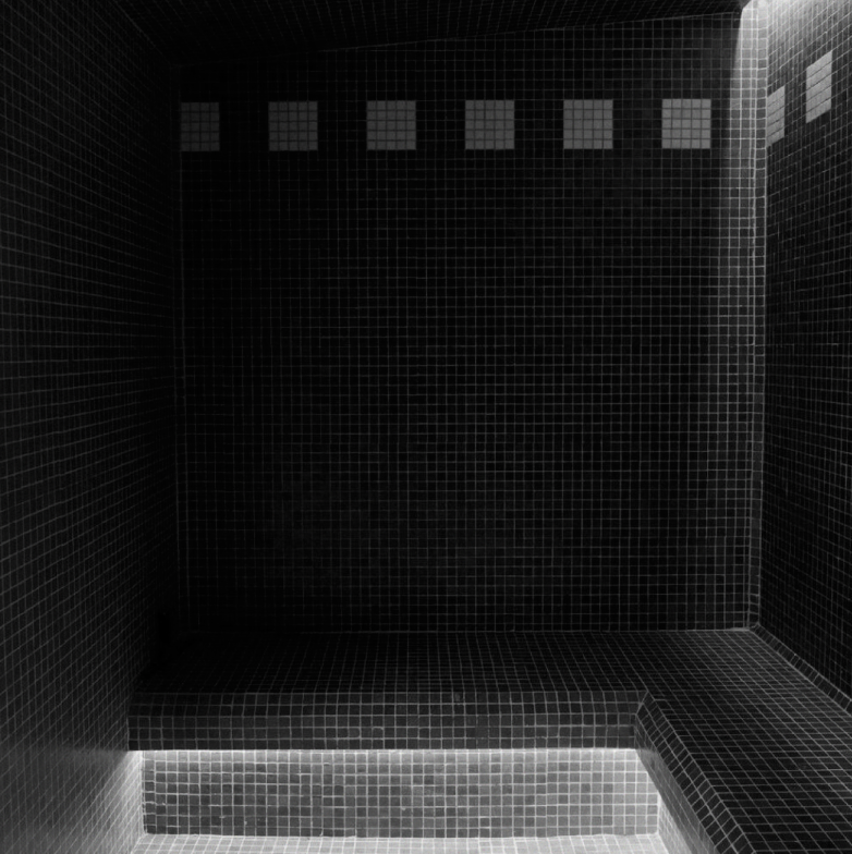 Dark tiled shower with a row of small square windows near the ceiling and an illuminated step or seating area at the bottom.
