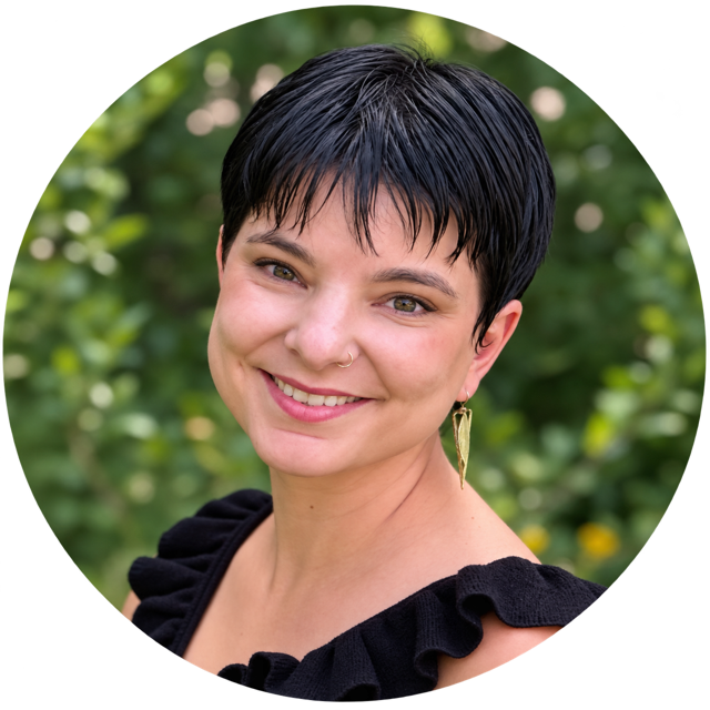 A woman with short black hair smiling outdoors, wearing a black top with ruffled sleeves and a gold leaf earring.