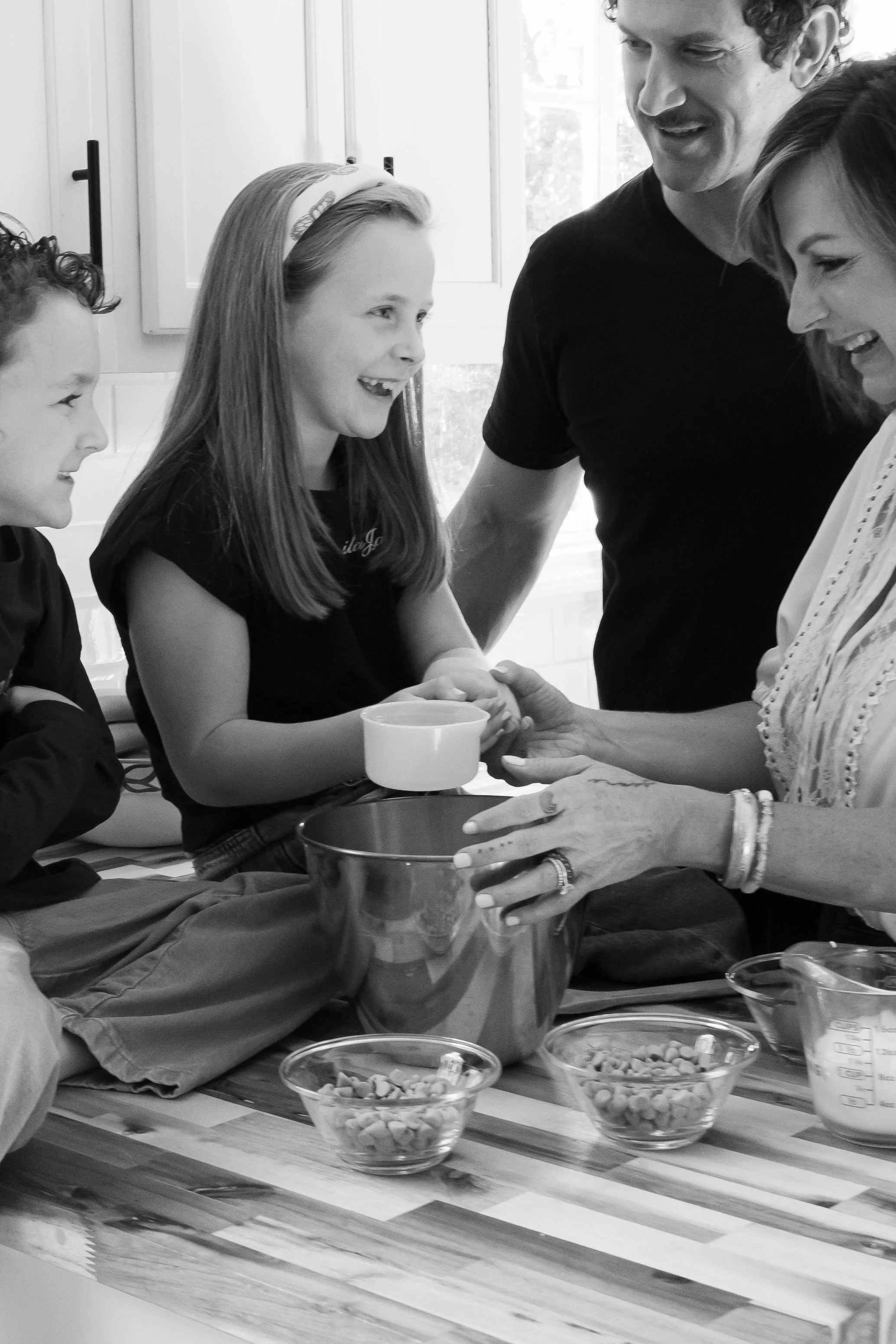 Four people gather around a table with bowls of nuts, smiling and engaged in conversation.