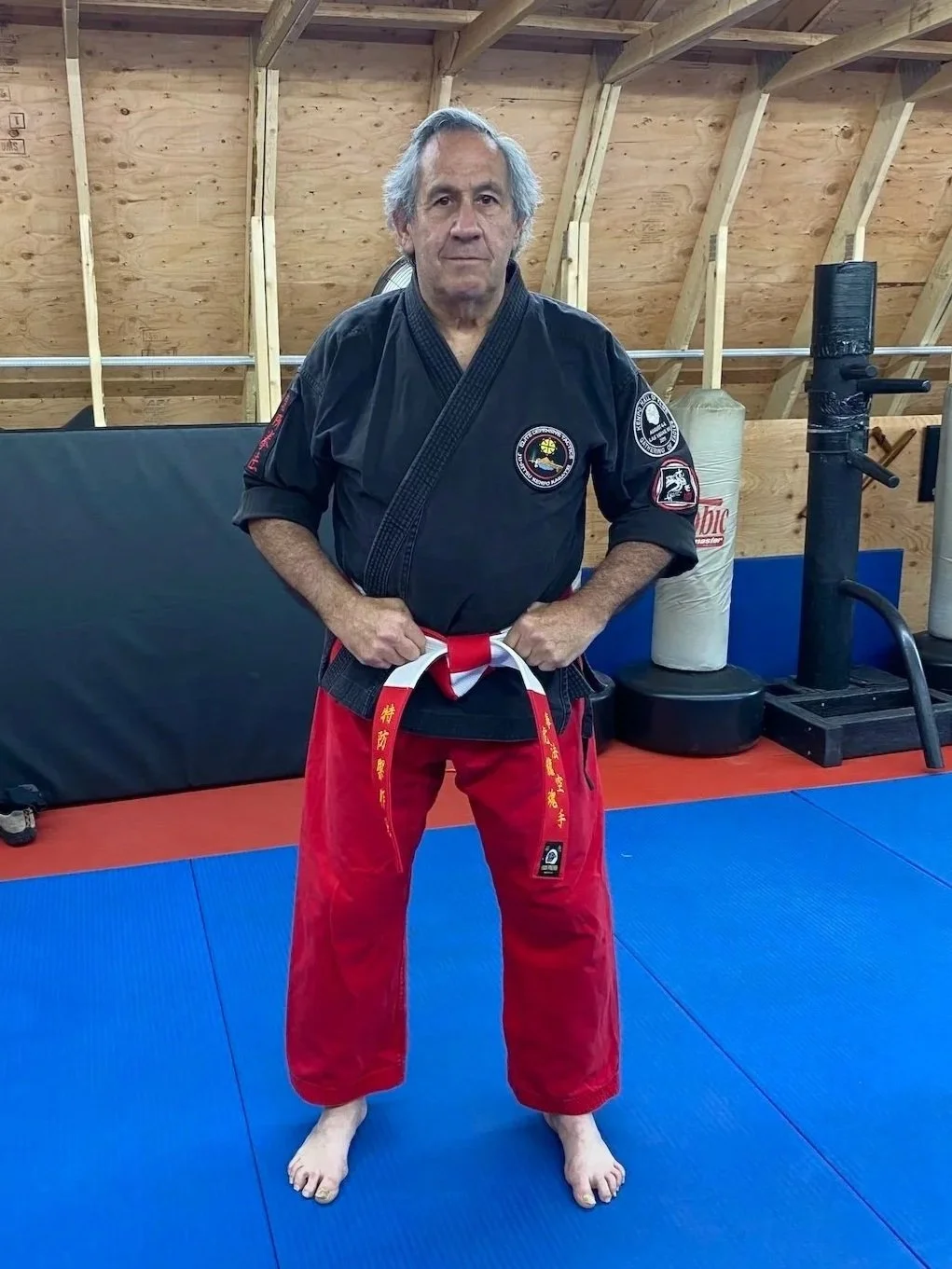 Roy Abramowitz wearing a black martial arts jacket and red trousers in a training studio.