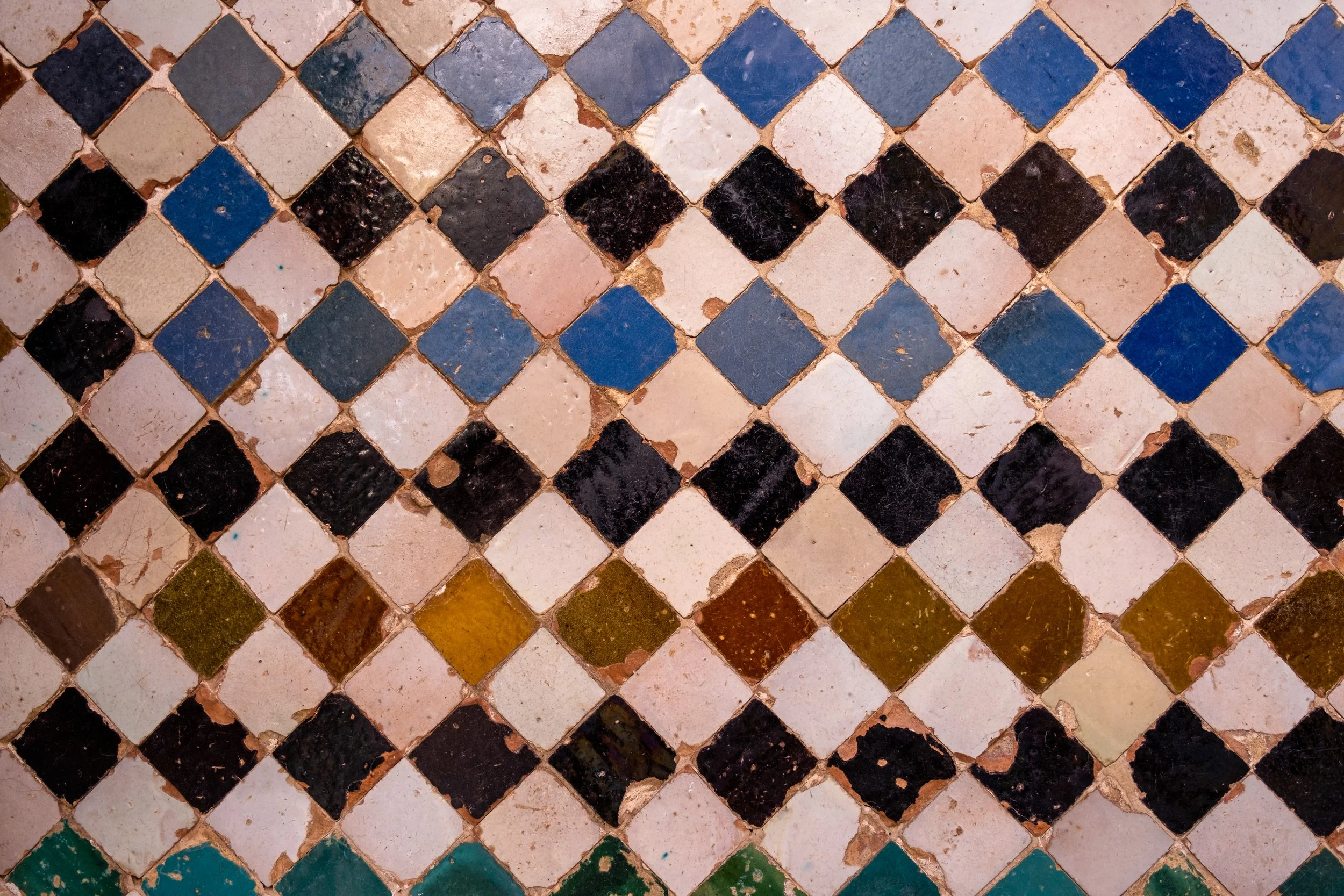 Carrelage de sol composé de petits carreaux colorés en bleu, noir, beige, vert et autres couleurs, disposés en motif diagonal.