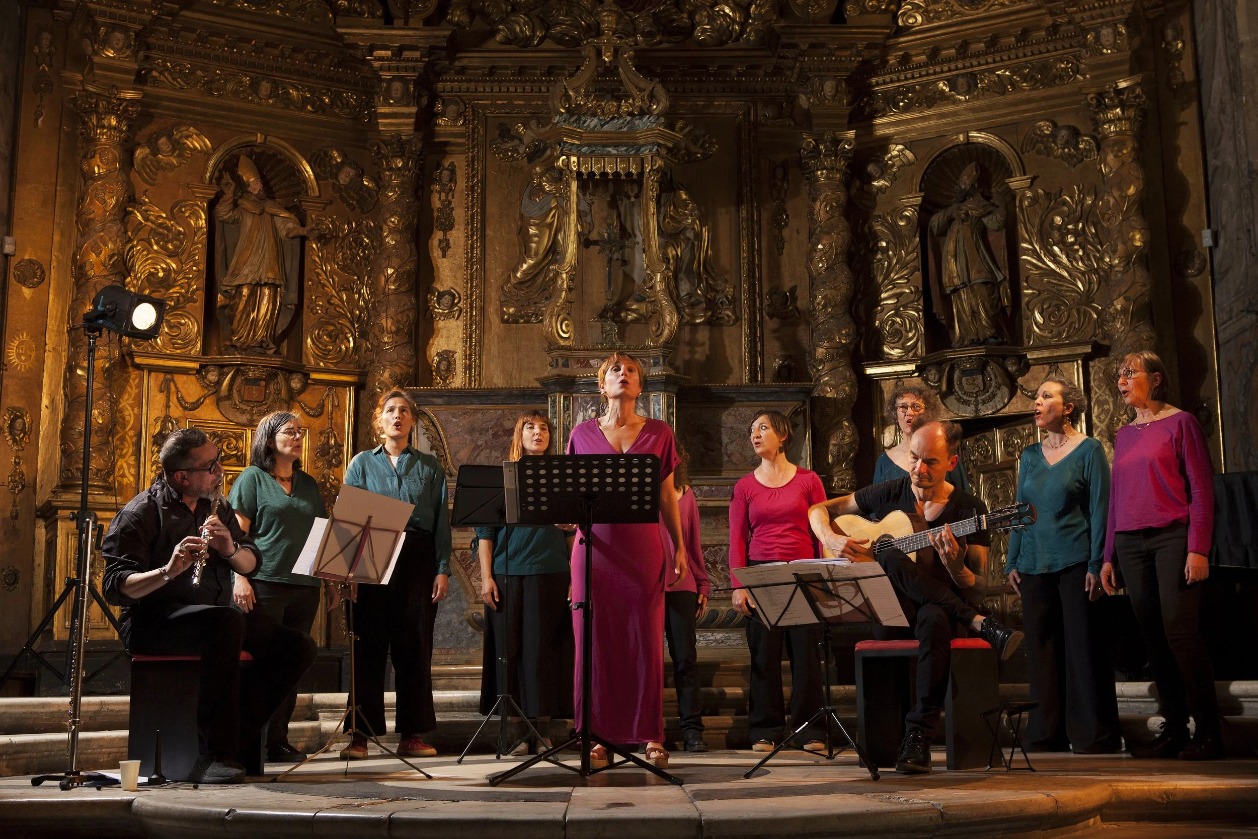Un groupe de chanteurs et musiciens se produisent lors d'une performance dans une salle ornée de décoration baroque dorée.
