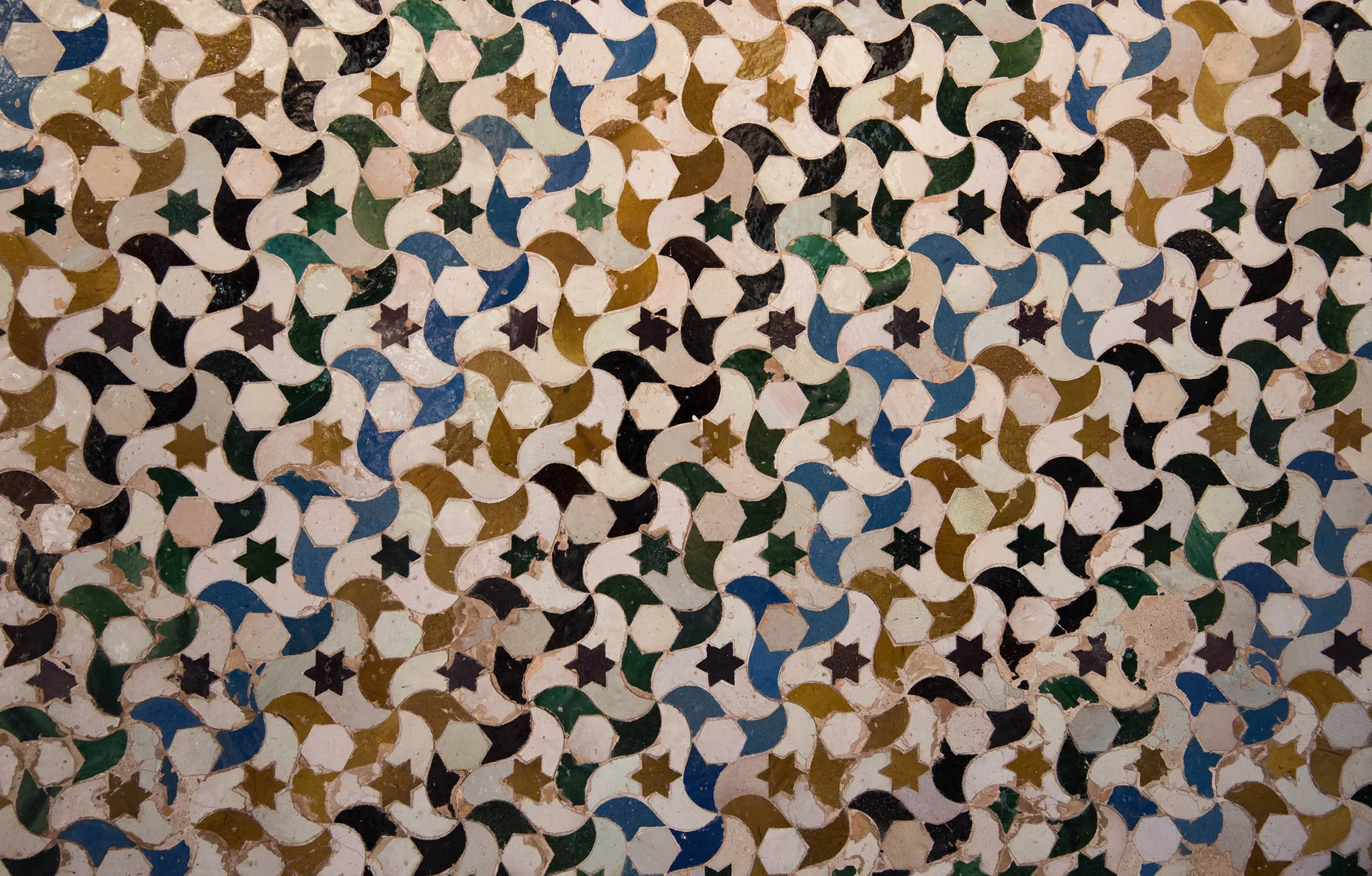Décoration murale composée de petits carreaux en céramique de différentes couleurs et formes, formant un motif géométrique répétitif.