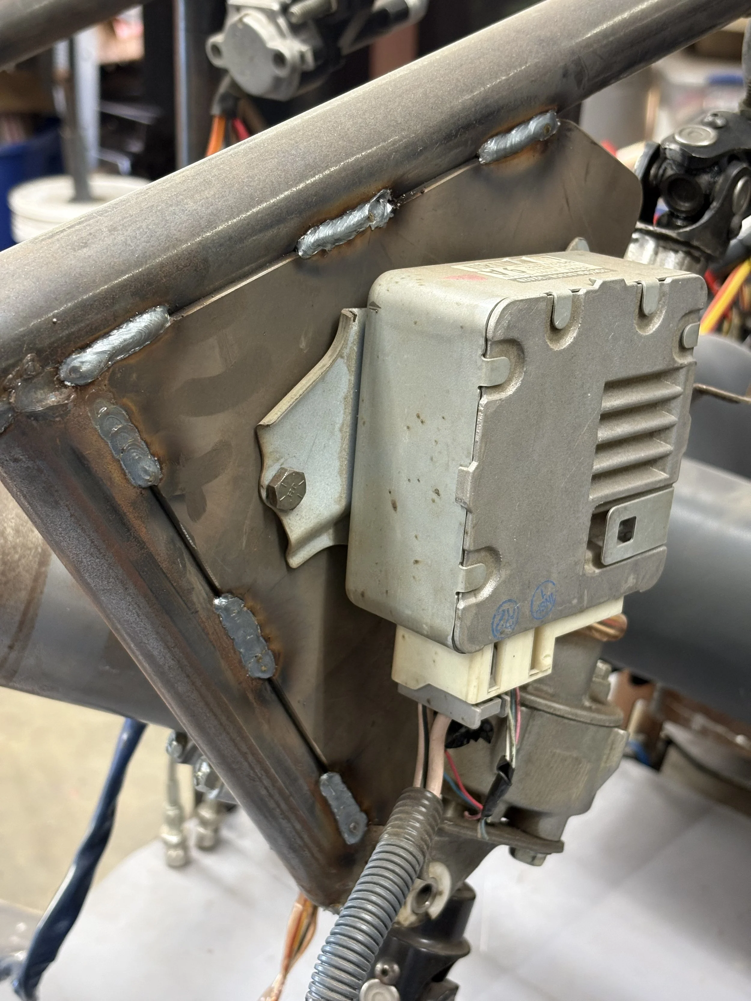 Close-up of a metal component with several welding spots, attached to an electronic control module with multiple wires, part of an industrial or mechanical system.