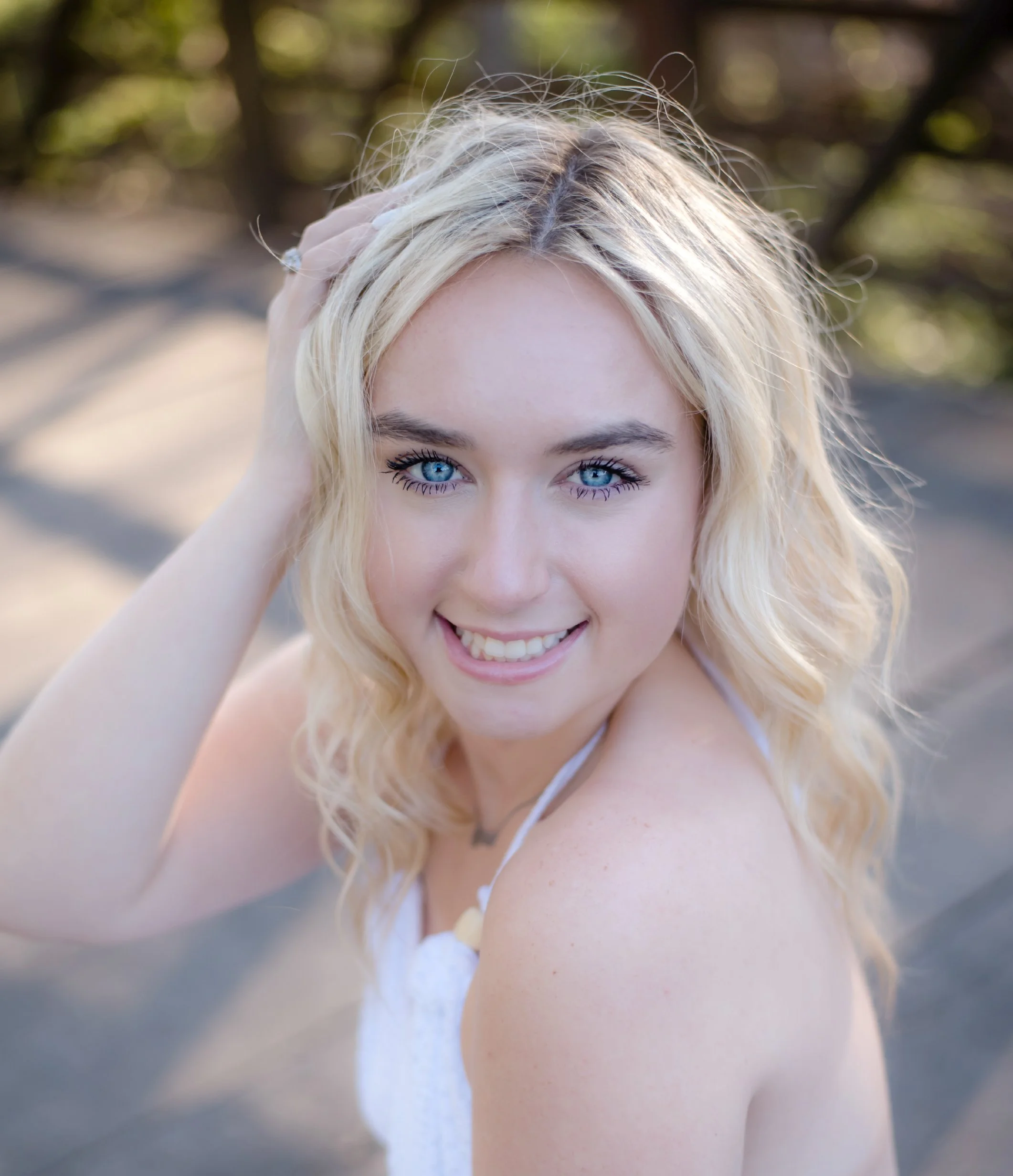 Close-up of a young woman with blue eyes and blonde hair, smiling, outdoors on a sunny day.
