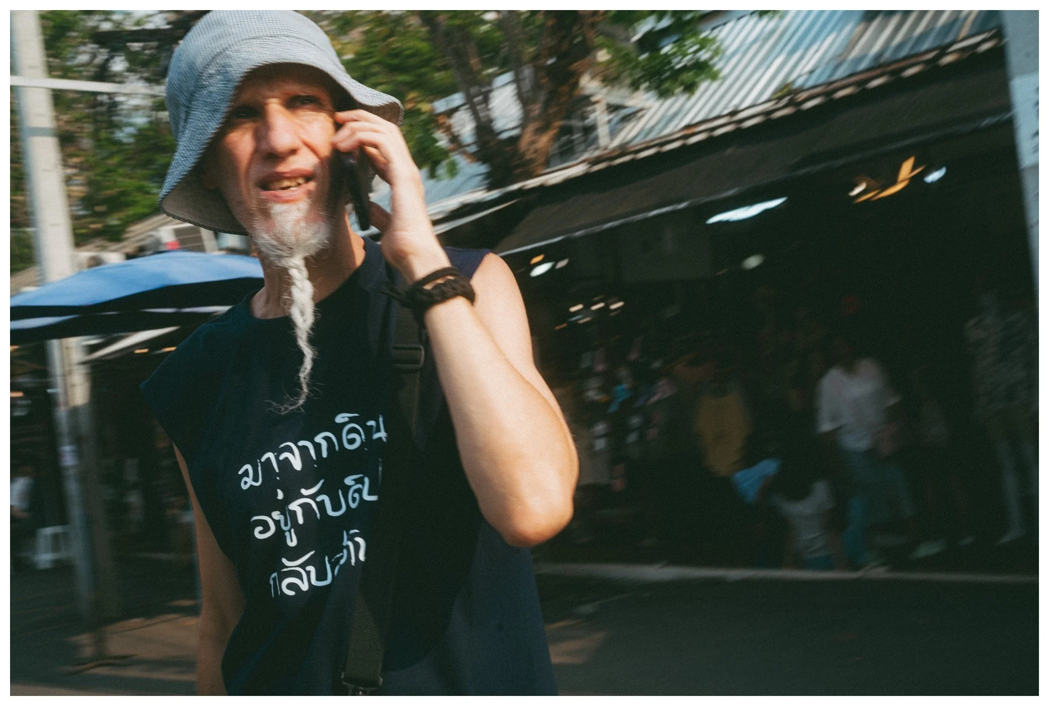 A person wearing a gray sun hat talking on a cellphone, with a blurred background of trees and a building.