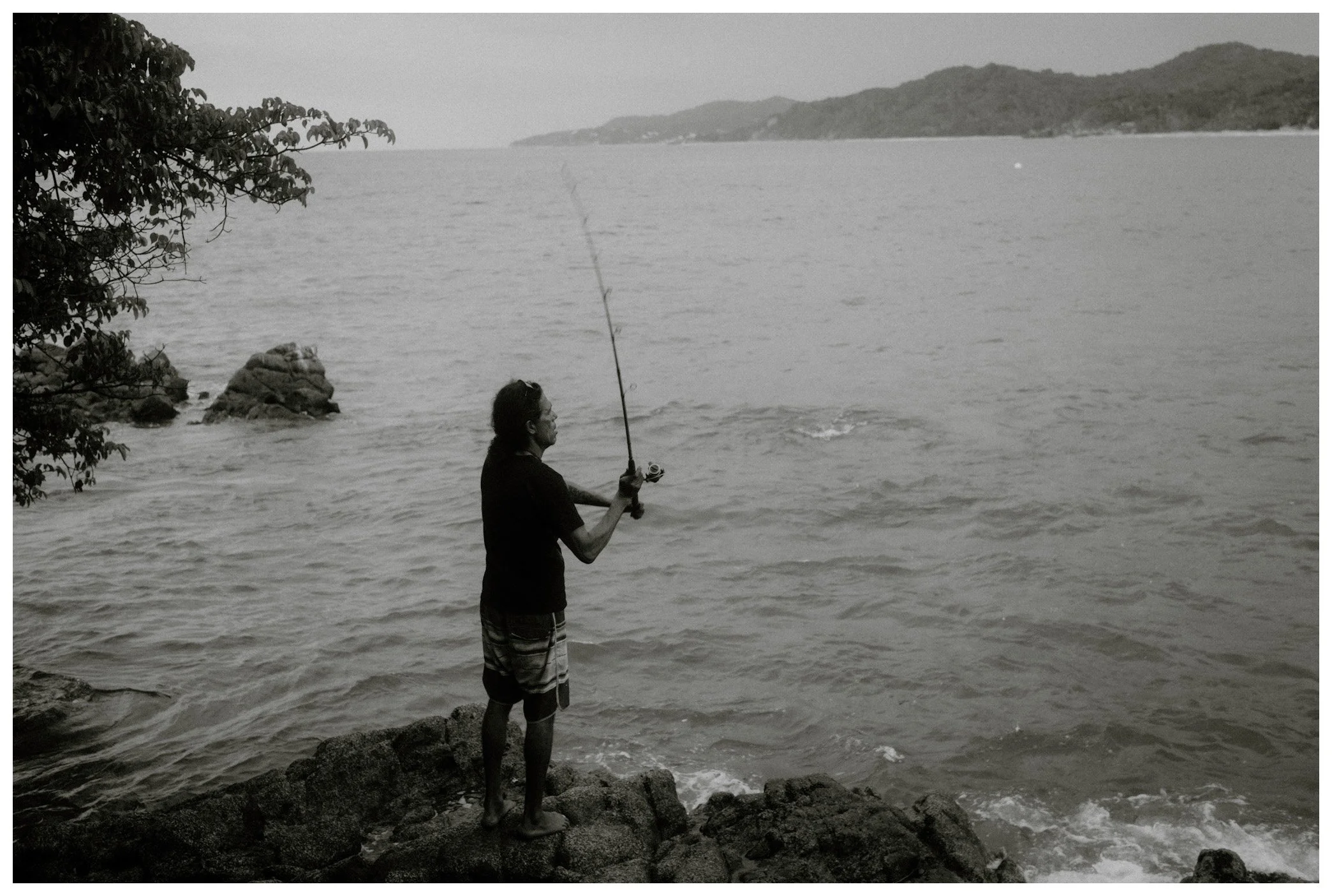 A man standing on rocks at the edge of a body of water, fishing with a fishing rod.