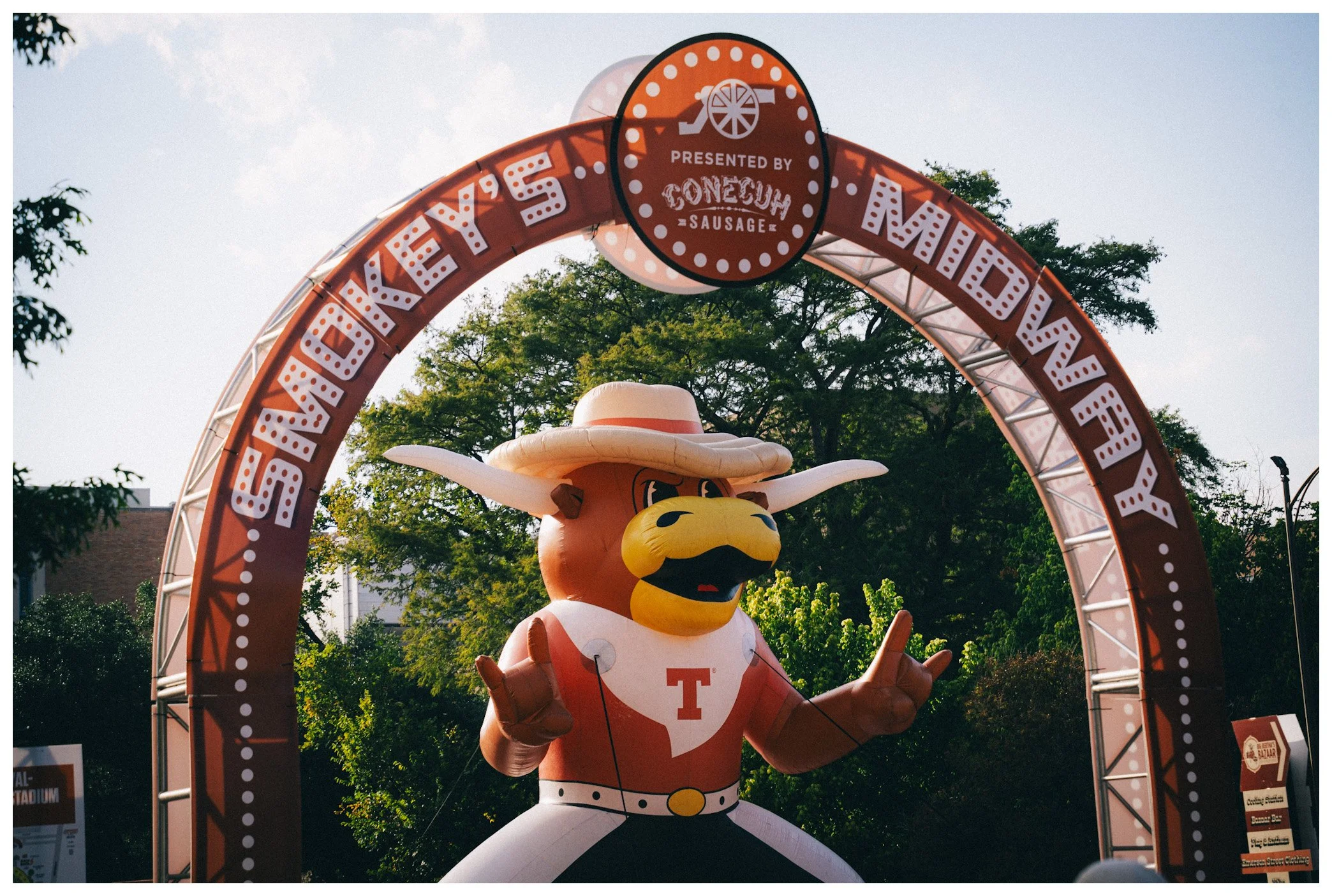 Inflatable mascot dressed in a University of Tennessee outfit at a fair or event, located under a red archway with white text and logo.”}