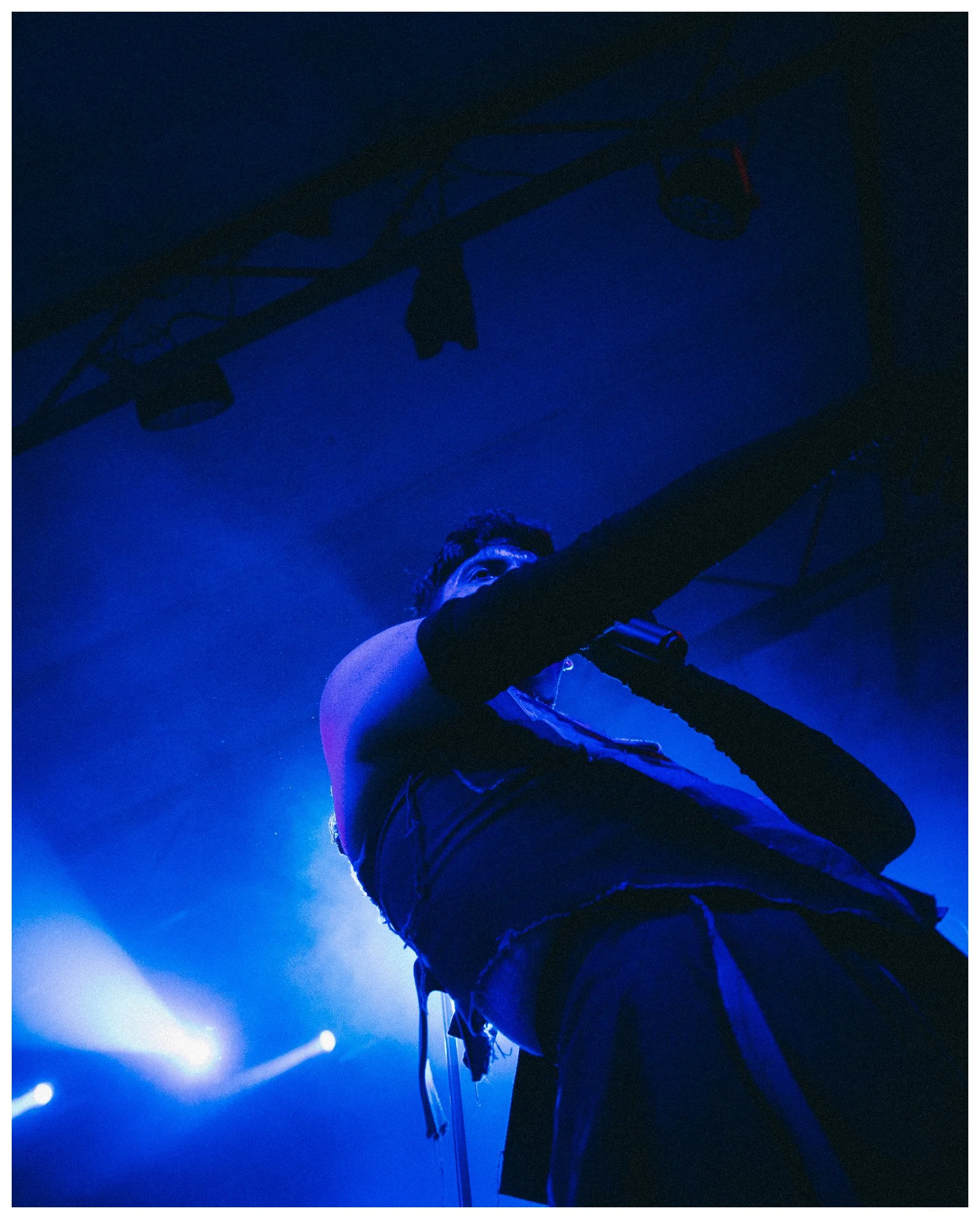 Person performing on stage under blue lighting, hold a microphone and wearing a sleeveless shirt.