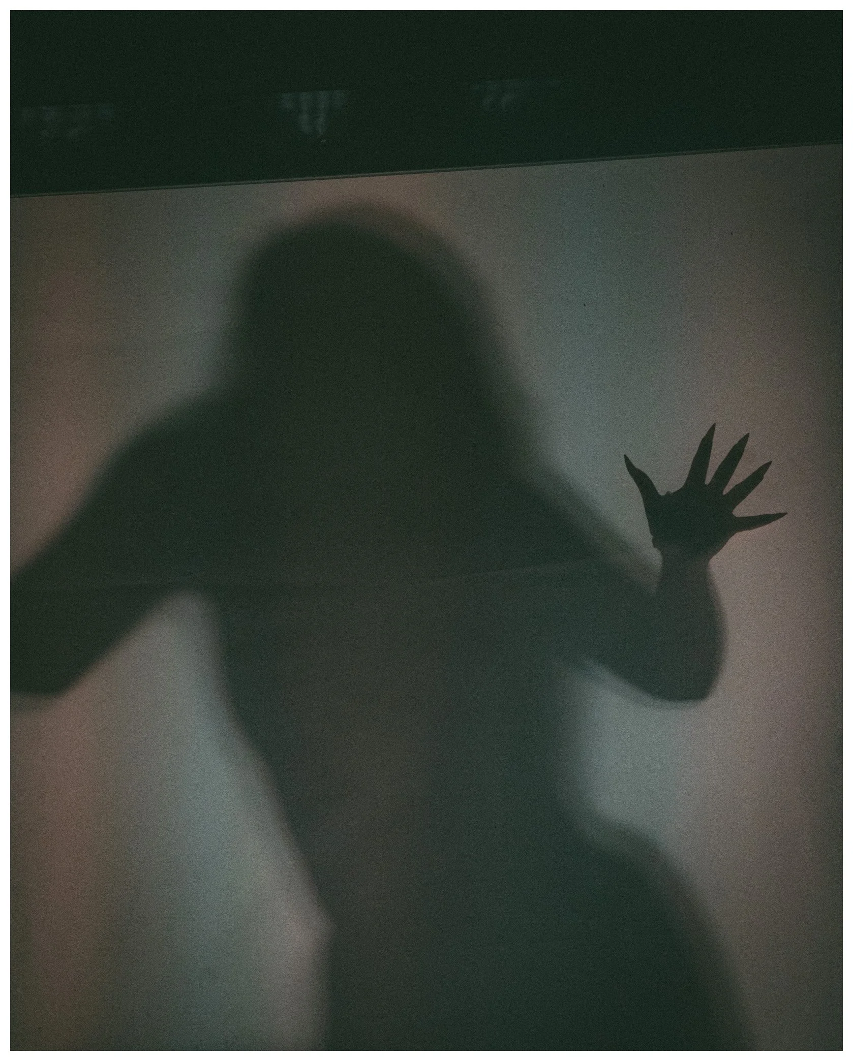 The image shows a silhouette of a hand with fingers spread against a surface, with a shadowy figure of a head and the surface above it, which appears to be a wall or ceiling, visible in the background.