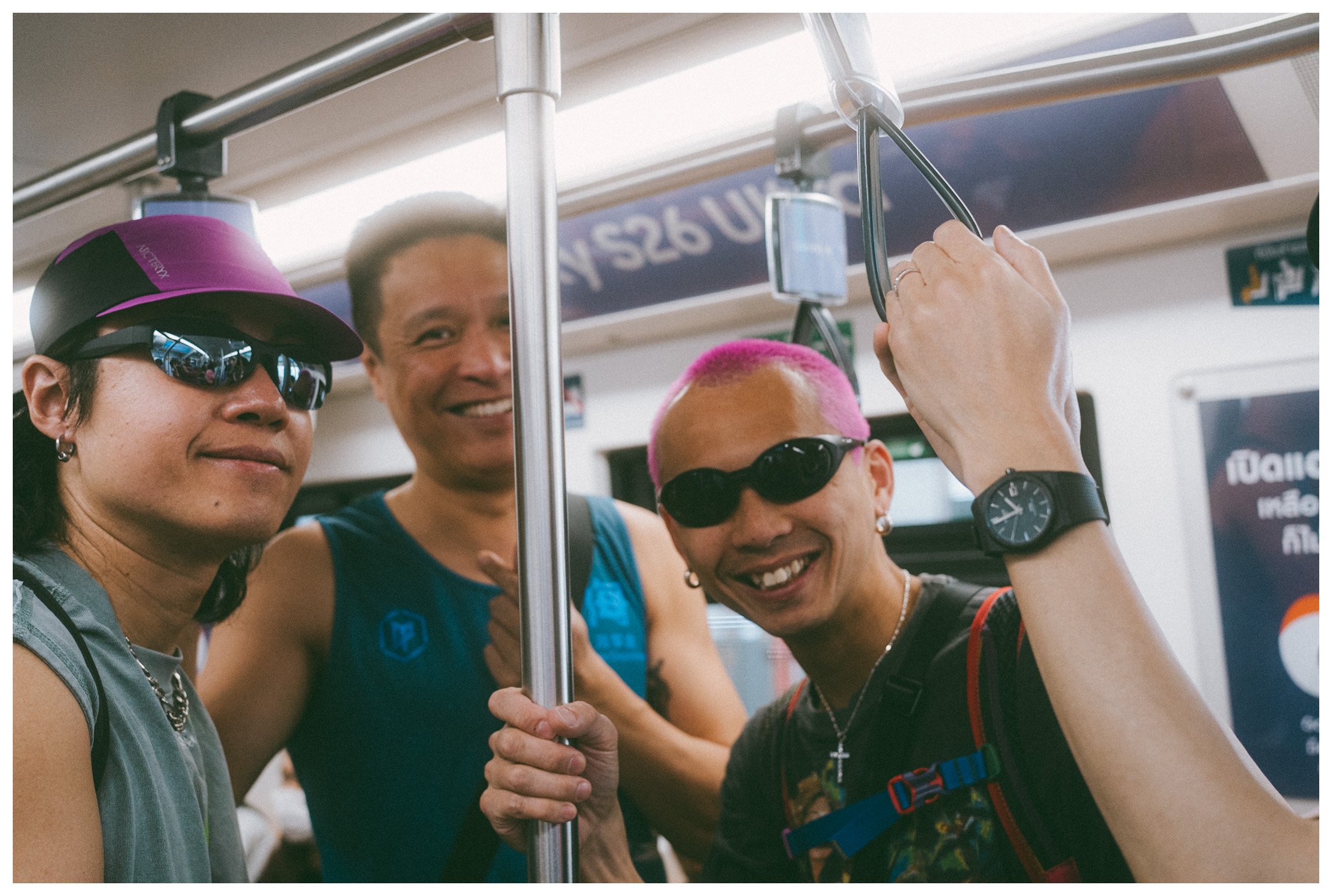 Four diverse people smiling and taking a photo together on a train, with one person holding a vertical handrail.