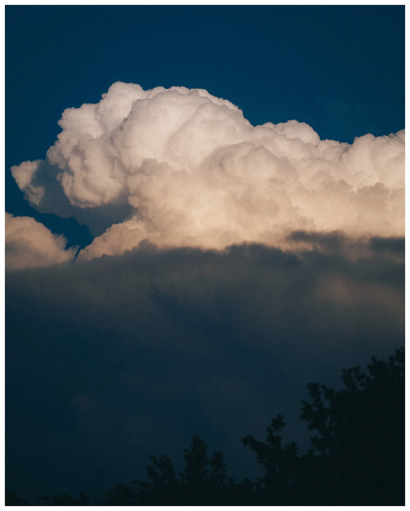 Night sky with large, billowing white clouds and a silhouette of trees at the bottom.